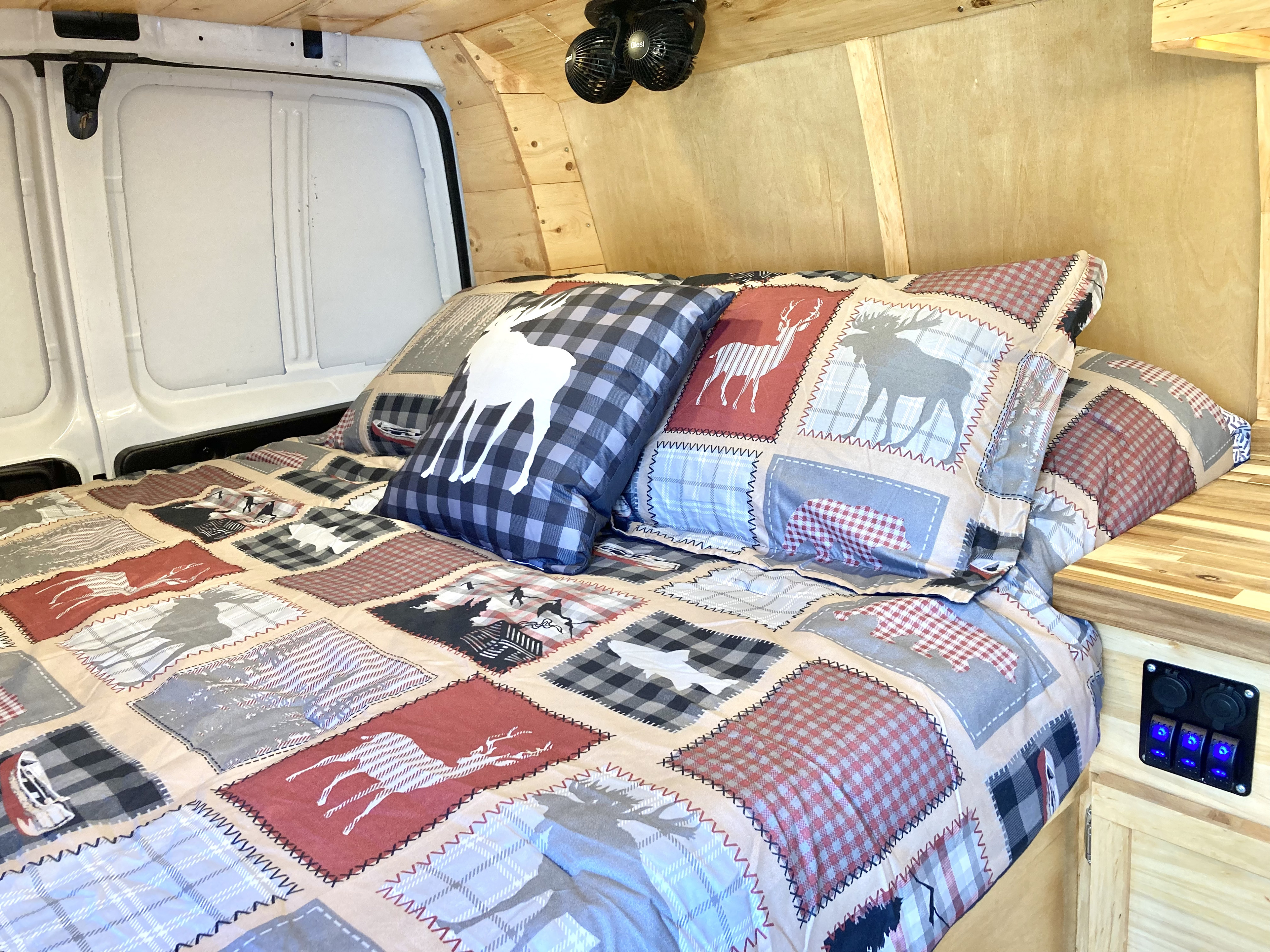 Cozy RV rental bed featuring a rustic patchwork comforter with animal motifs, wood-paneled walls, and ceiling fans.. Ford Econoline 2012