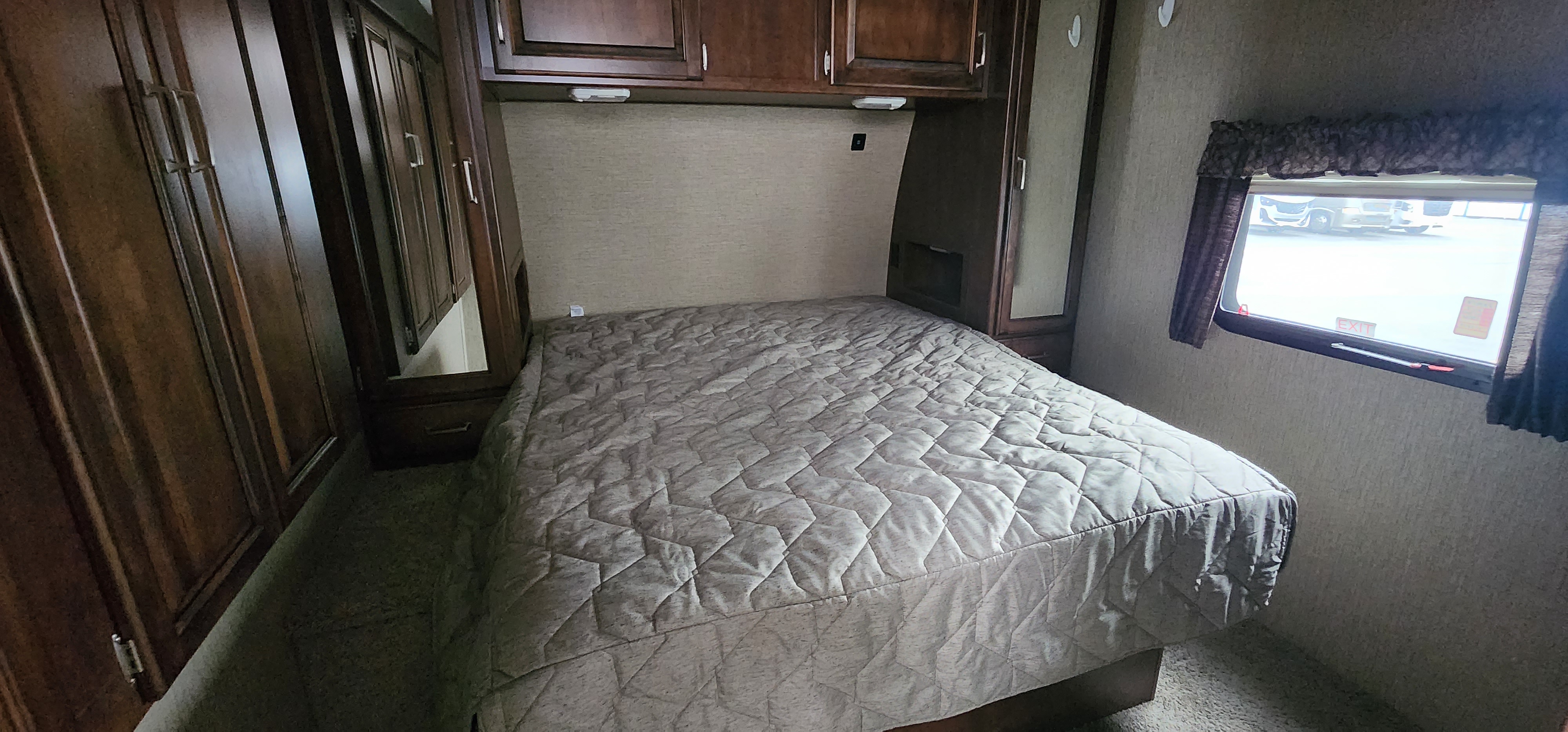 Inside a compact RV rental bedroom featuring a comfy bed, overhead cabinets, and a window.. Keystone RV Outback Super-Lite 2017