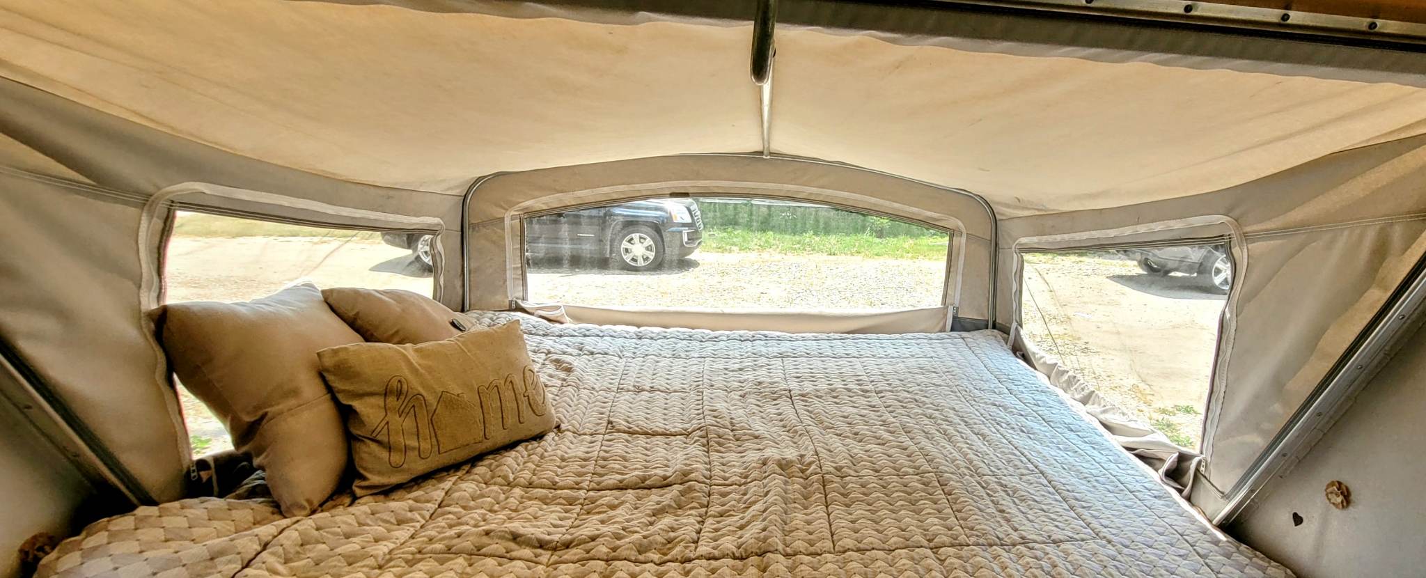 Inside a cozy RV rental pop-up camper. Features a comfy bed with pillows and a clear view of the outdoors.. Other Other 1998