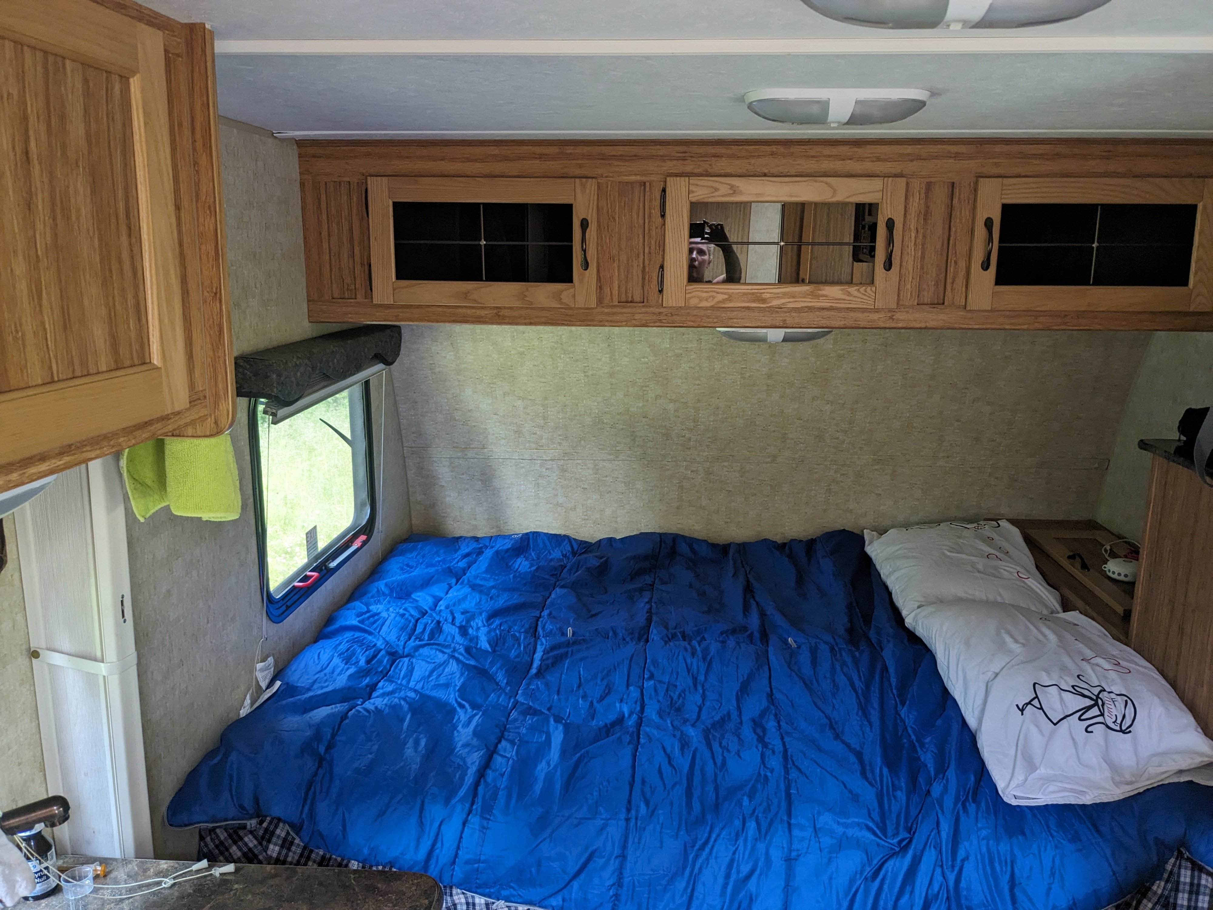 Cozy bedroom inside an RV rental, featuring a bed with blue bedding, wooden cabinets, and a window with green views.. Skyline KOALA 18RB 2012