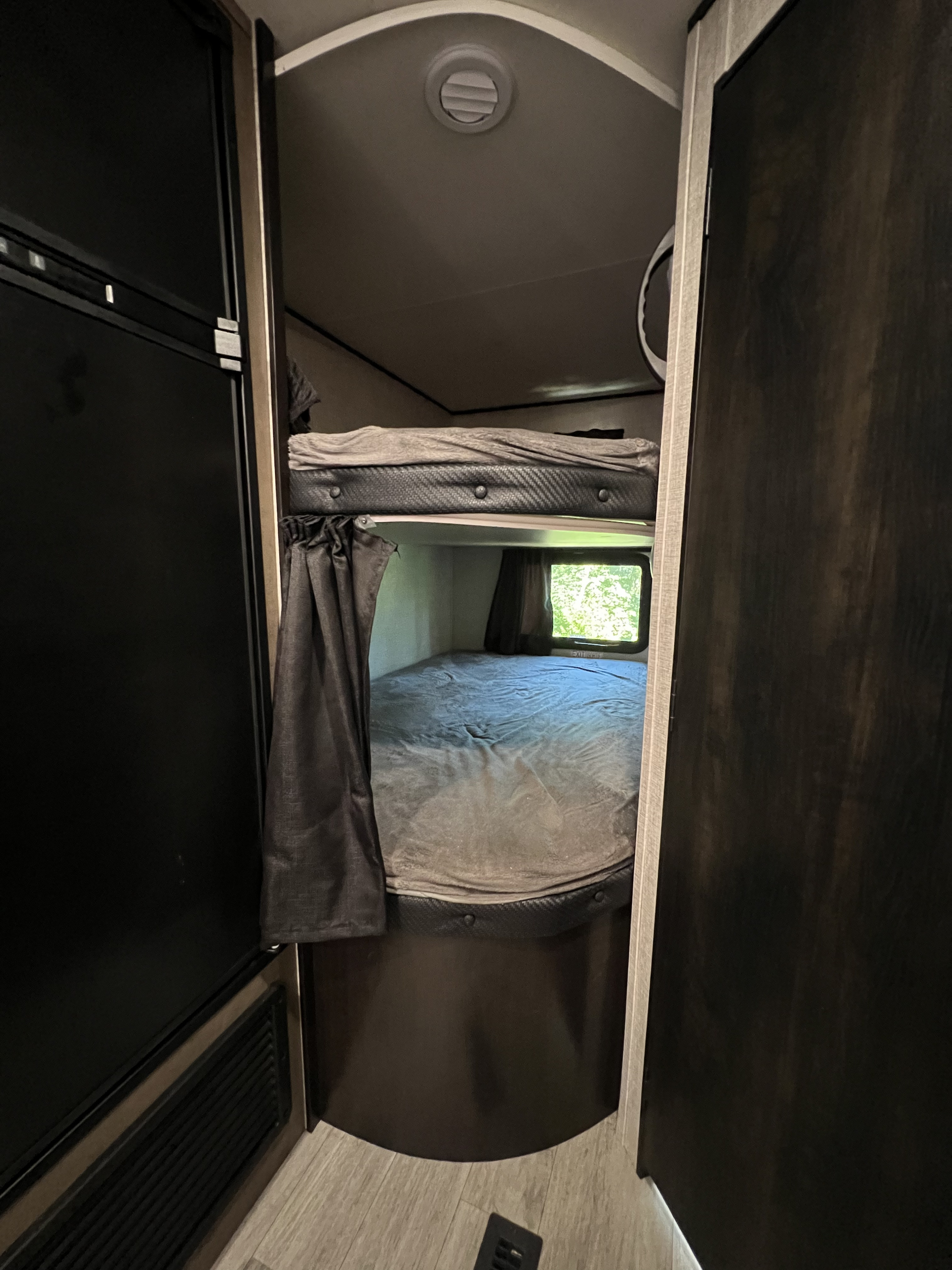 Interior view of an RV rental showing cozy bunk beds with curtains, a window with outdoor greenery, and a ceiling vent.. Jayco Jay Flight SLX Rocky Mountain Edition 2022