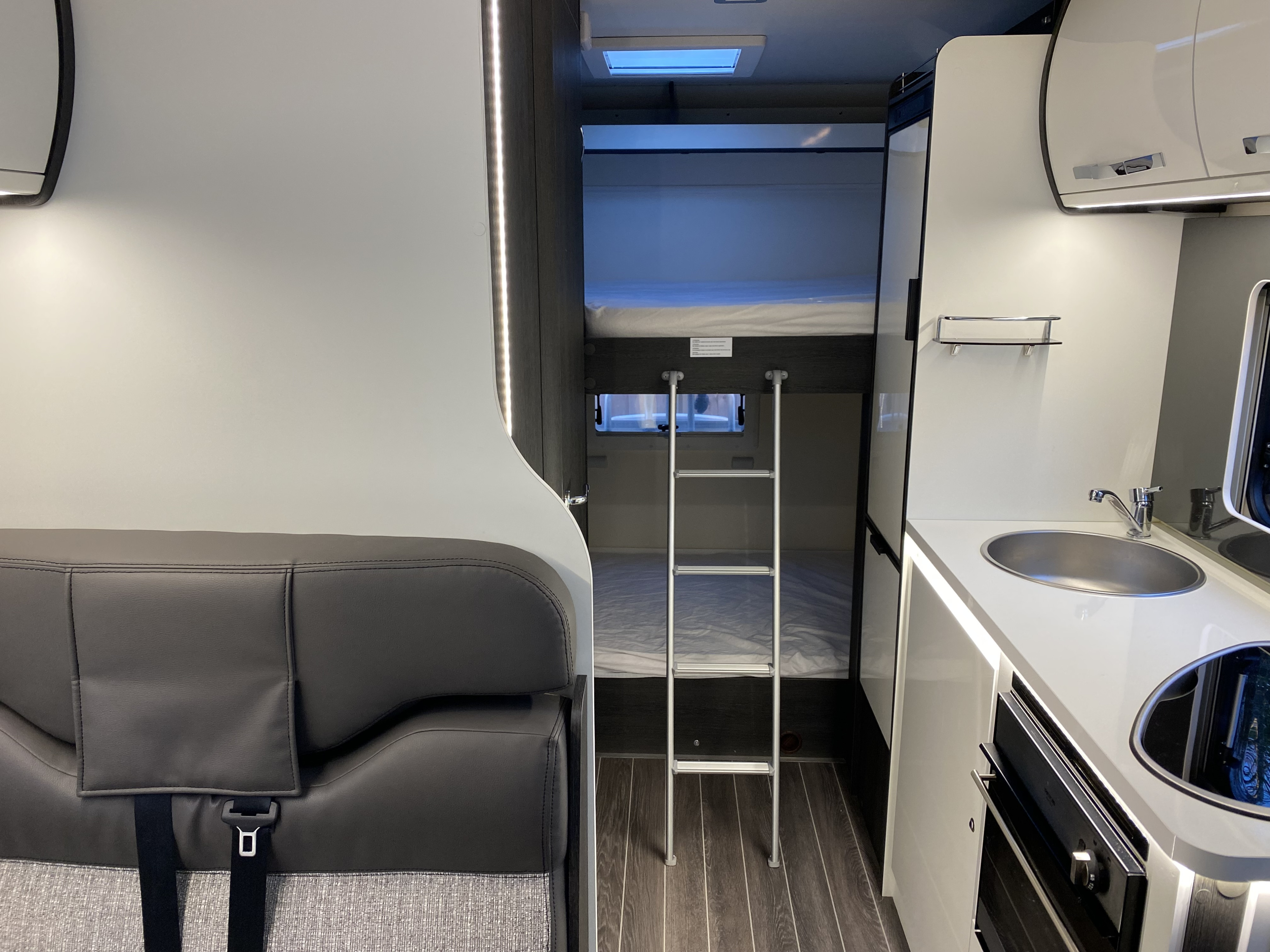 Modern RV rental interior: bunk beds, kitchenette with sink/cooktop, and lounge seating.. Ford Rollerteam Zefiro 675 2021