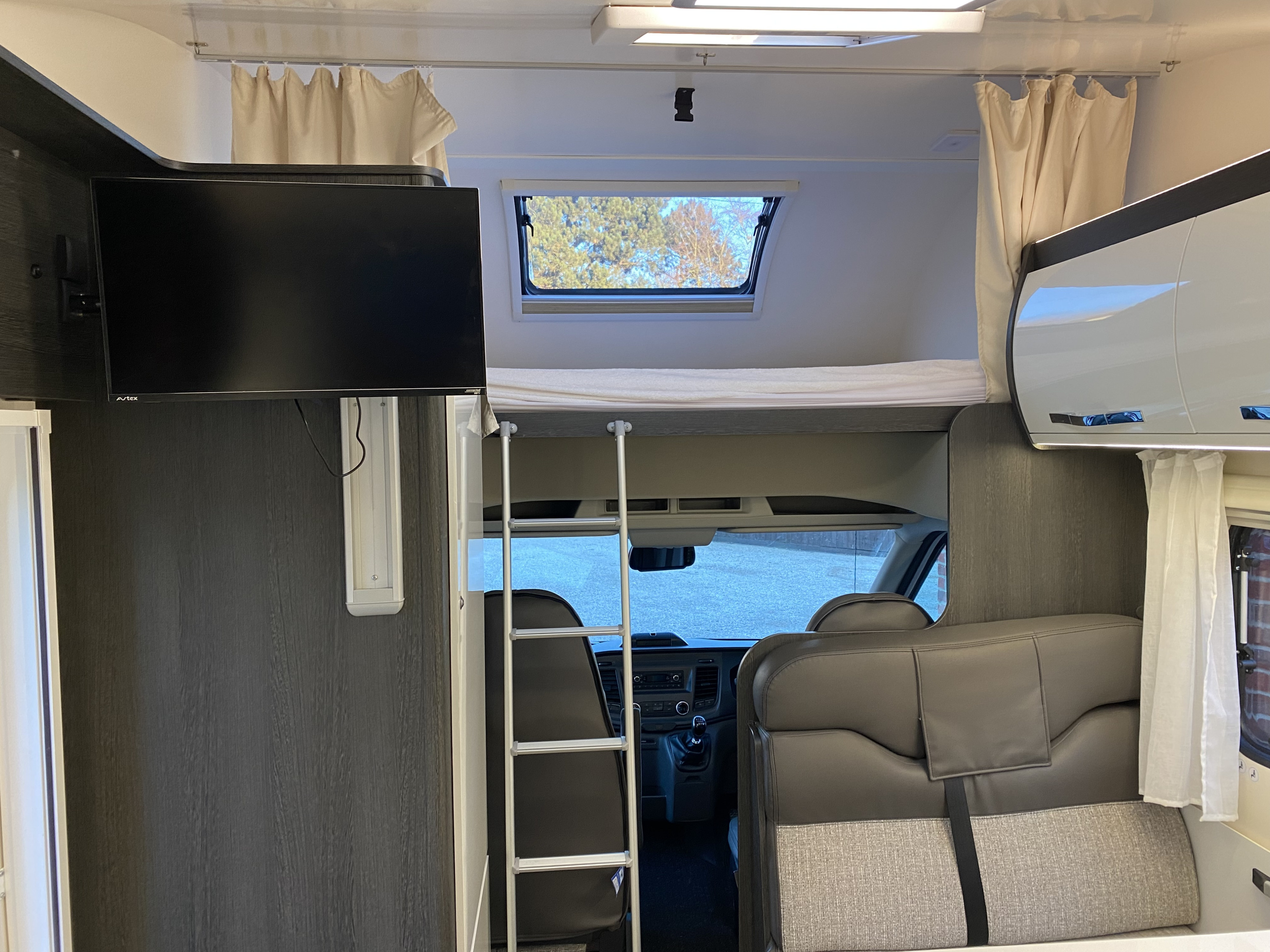 RV rental interior with a cozy bunk bed, access ladder, wall-mounted TV, and front cabin view.. Ford Rollerteam Zefiro 675 2021