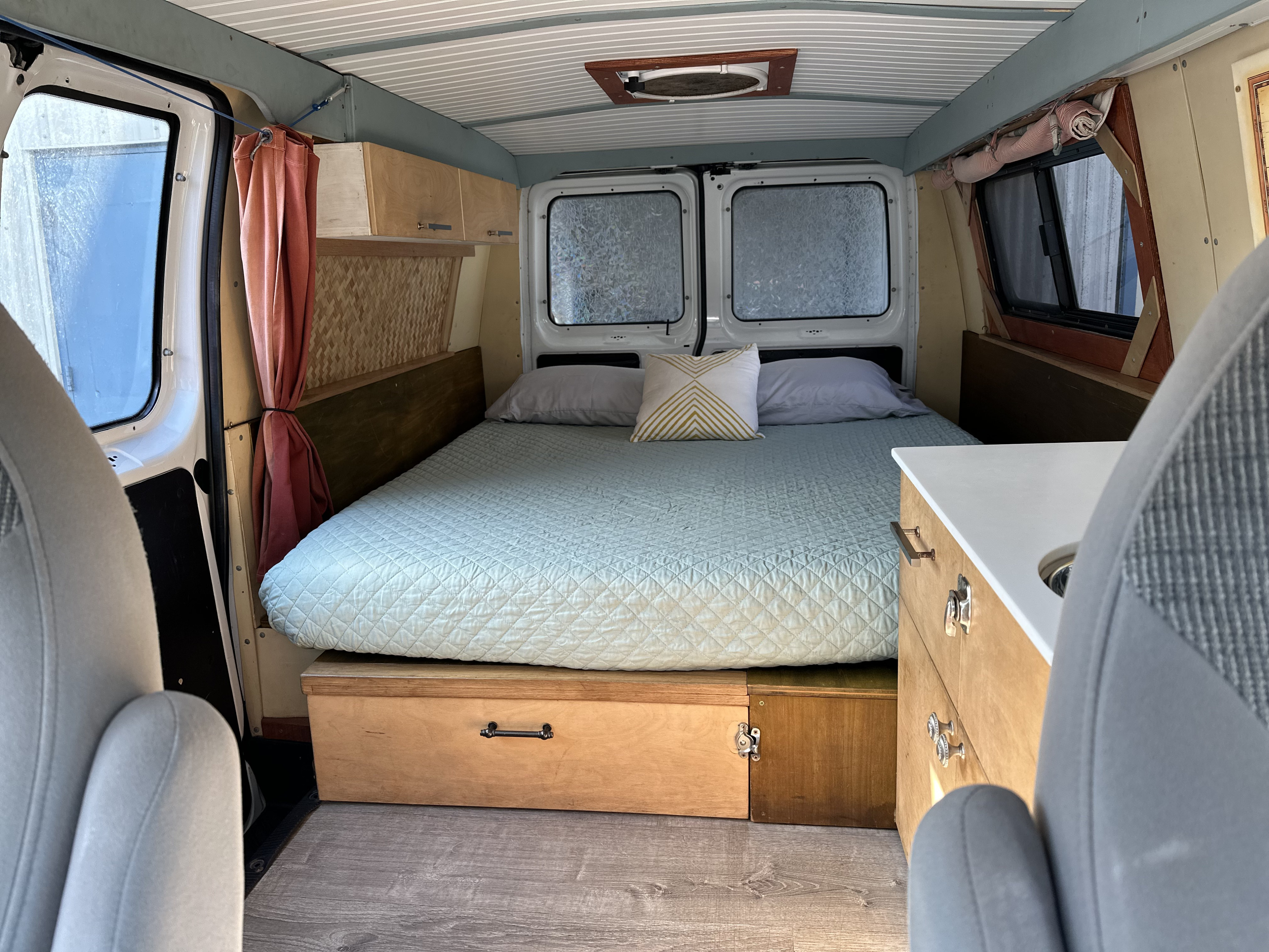 Inside a cozy rv rental camper van with a large bed, built-in storage, and small kitchen area.. Ford E150 2002