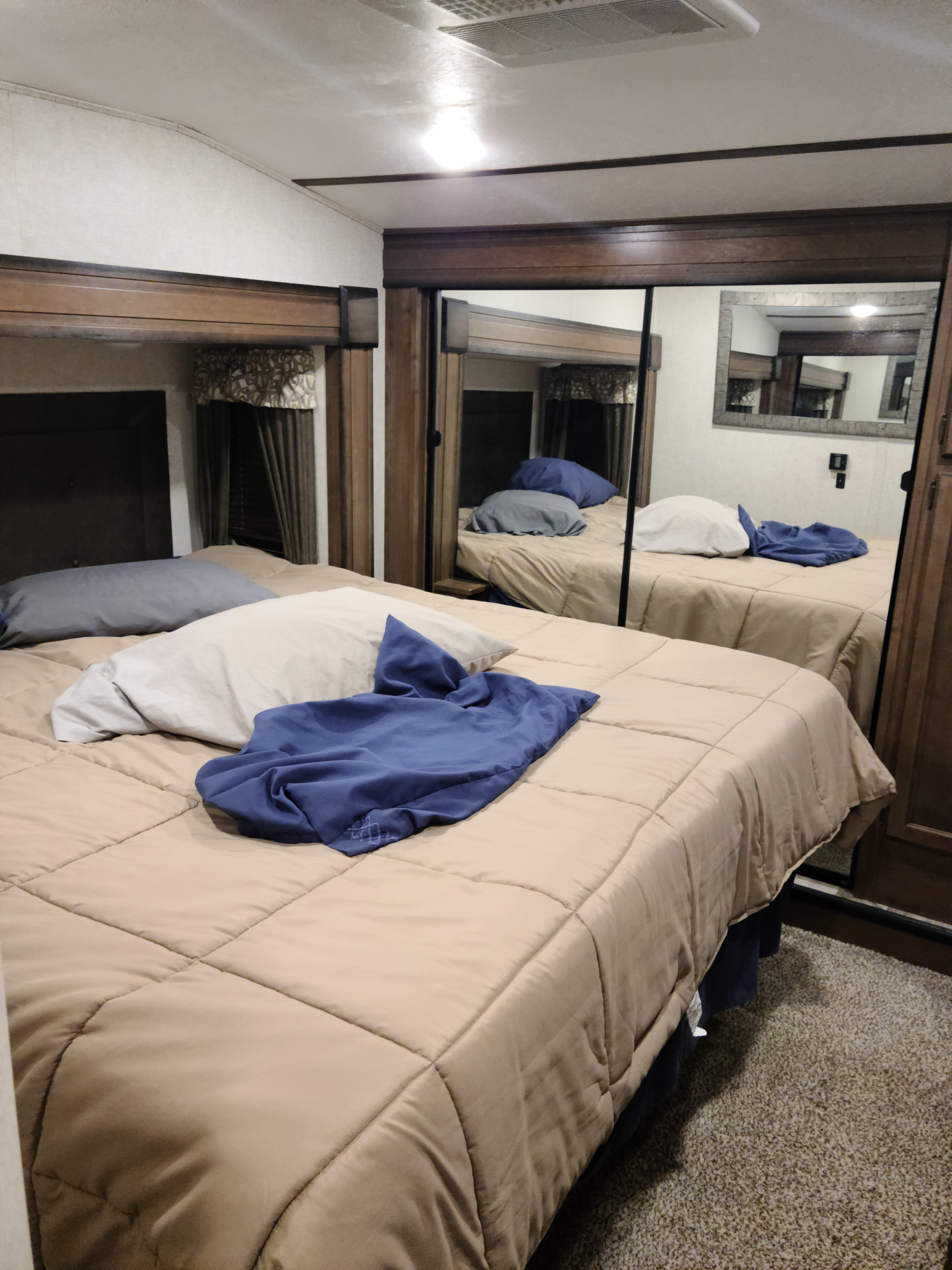 RV rental bedroom showcasing a comfortable bed with light comforter and pillows, plus a mirrored closet for storage.. Keystone RV Cougar 2018