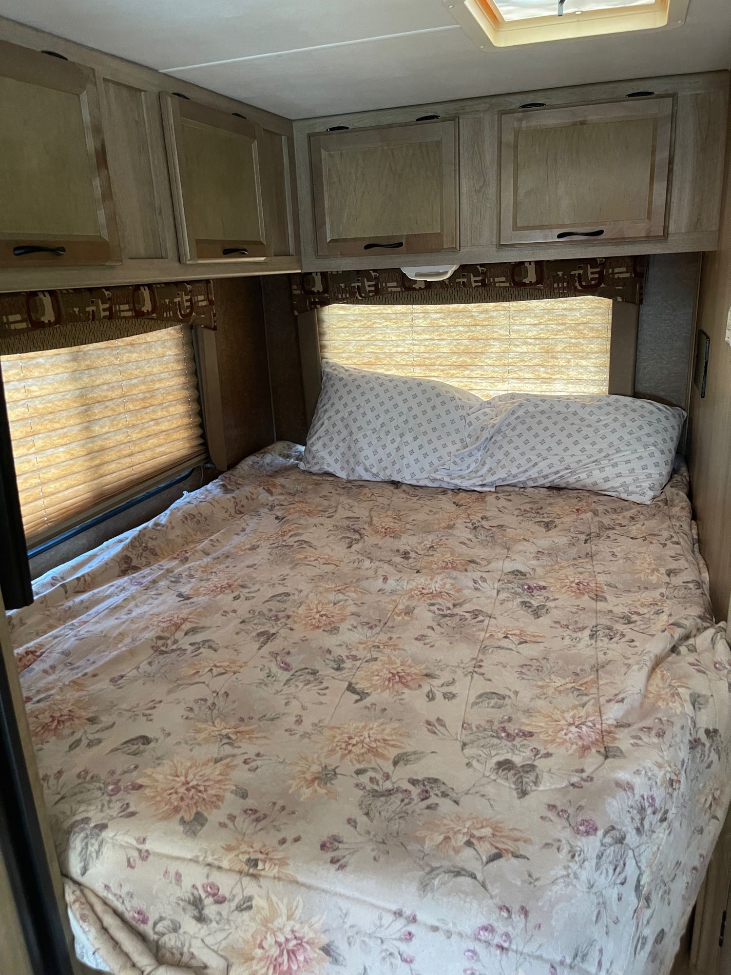 Cozy RV rental bedroom with floral bed, window blinds, and wooden overhead cabinets.. Forest River Coachmen Freelander 2014