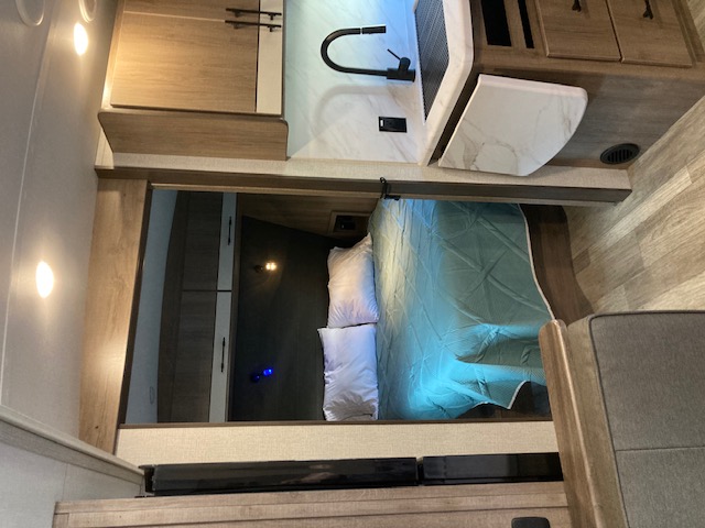 RV rental interior shows a compact bedroom (bed with blue comforter), kitchen with sink, and storage cabinets.. Grand Design Imagine 2023
