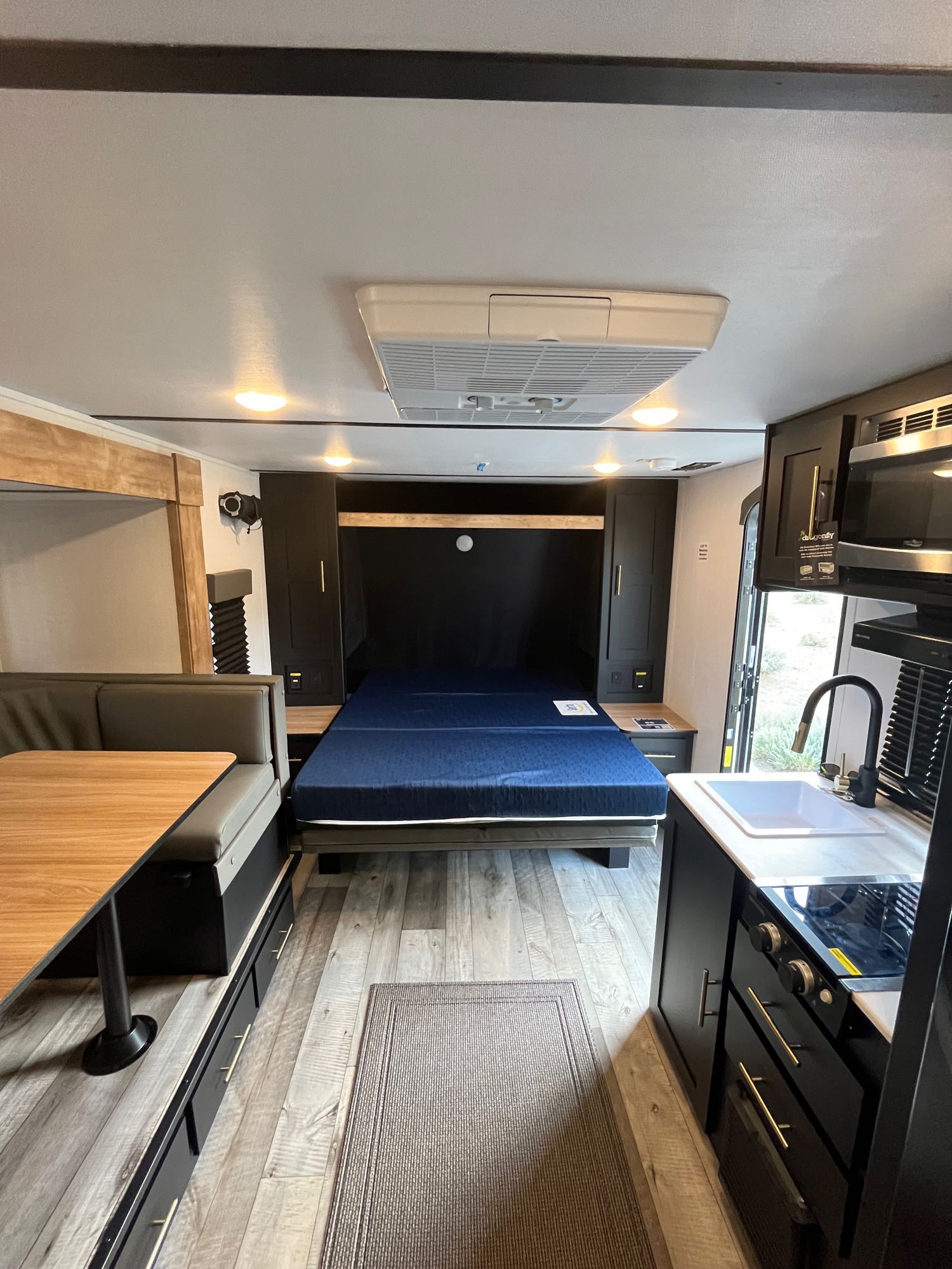 Modern RV rental interior showing a comfortable fold-down bed, dinette with storage, and a well-equipped kitchen area.. Keystone RV Springdale 2023