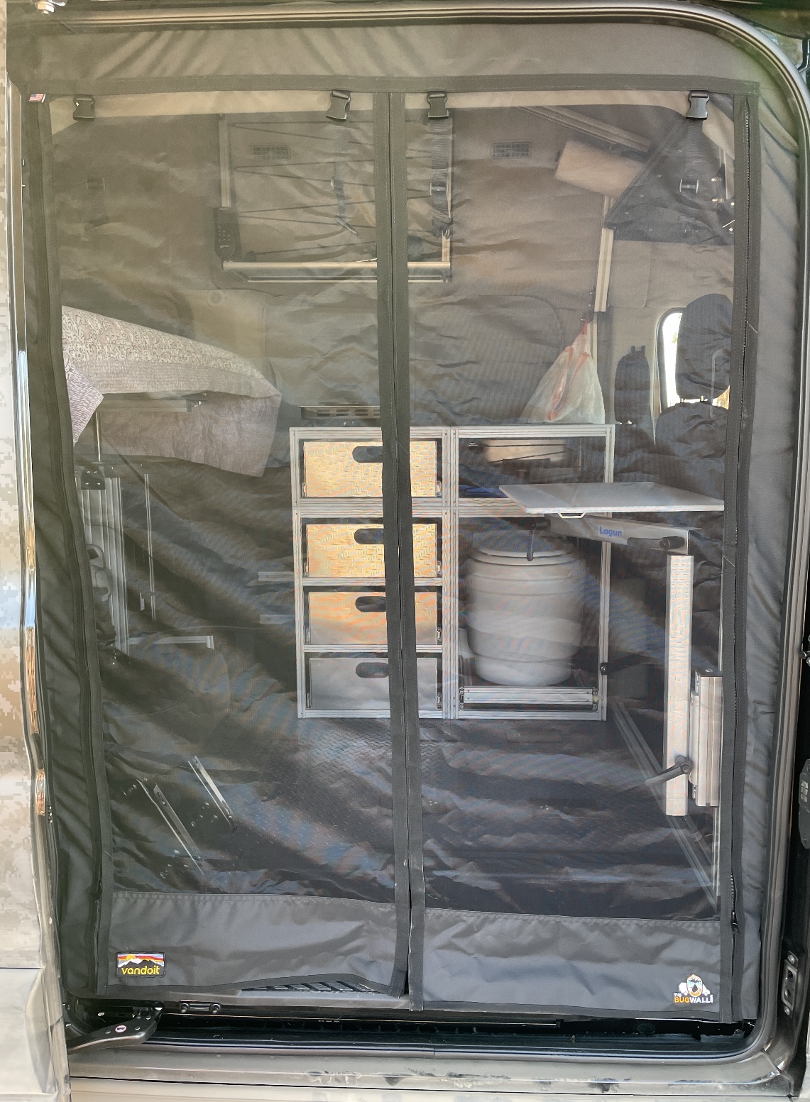 Inside an RV rental camper van, revealing organized storage, bed, and water tank through a black mesh screen door.. VanDoit Liv AWD Camper Van 2022