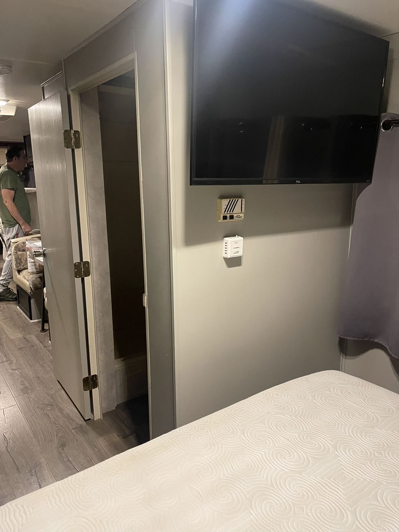 RV rental interior: bedroom area with mounted TV, climate controls. An open doorway reveals a man in the main living space.. Thor Motor Coach Four Winds Majestic 1996