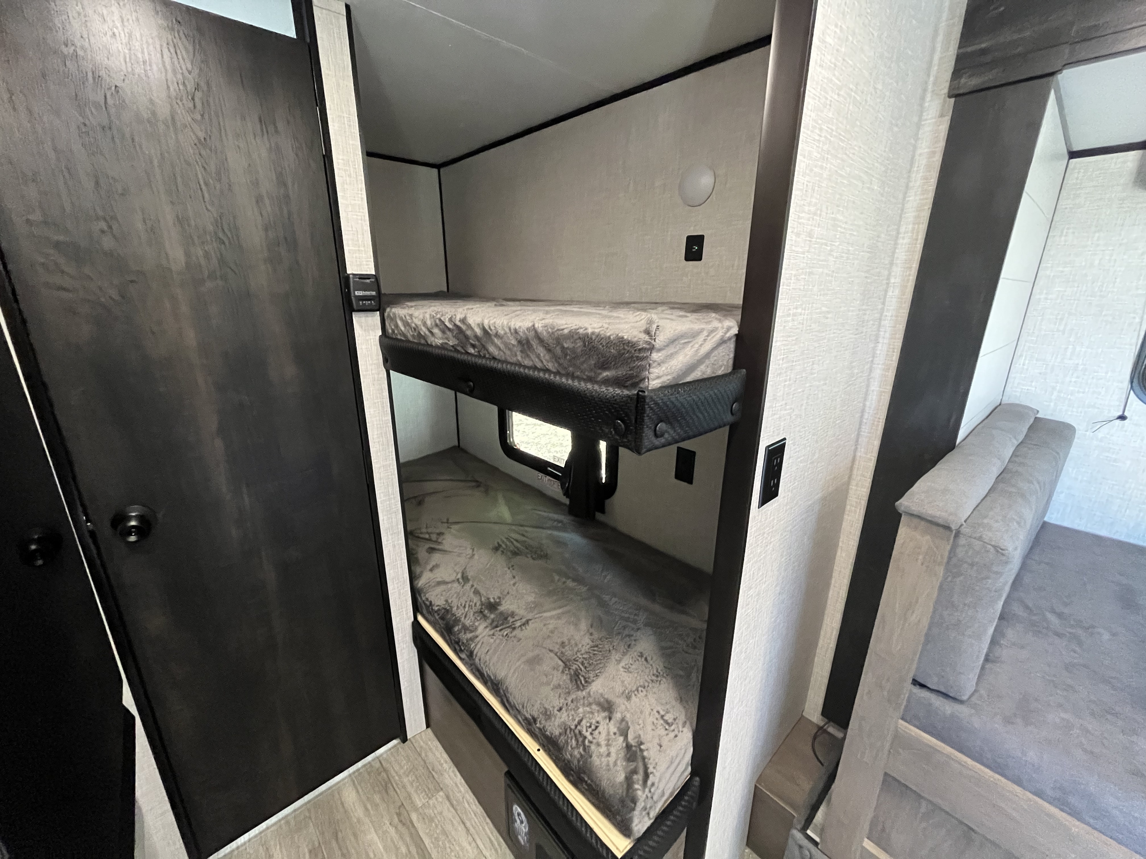 Inside an RV rental: a dedicated bunk bed area with two beds, a door to the left, and a light-colored sofa in the background.. Jayco Jay Flight SLX Baja Edition 2023