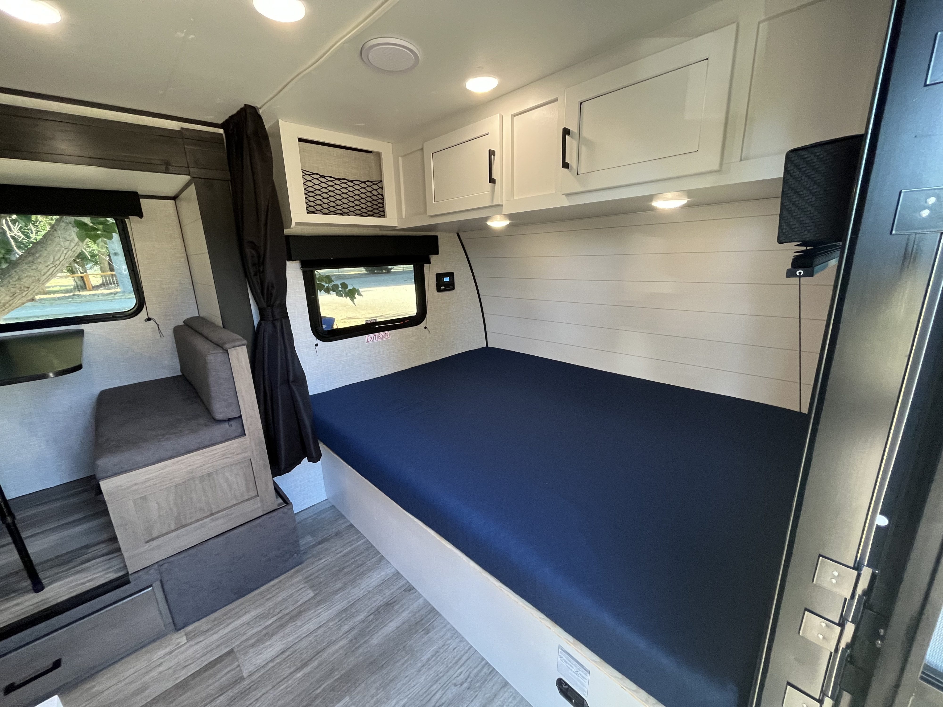 Inside a modern RV rental: cozy bedroom with blue bed, white shiplap wall, overhead cabinets, and seating.. Jayco Jay Flight SLX Baja Edition 2023
