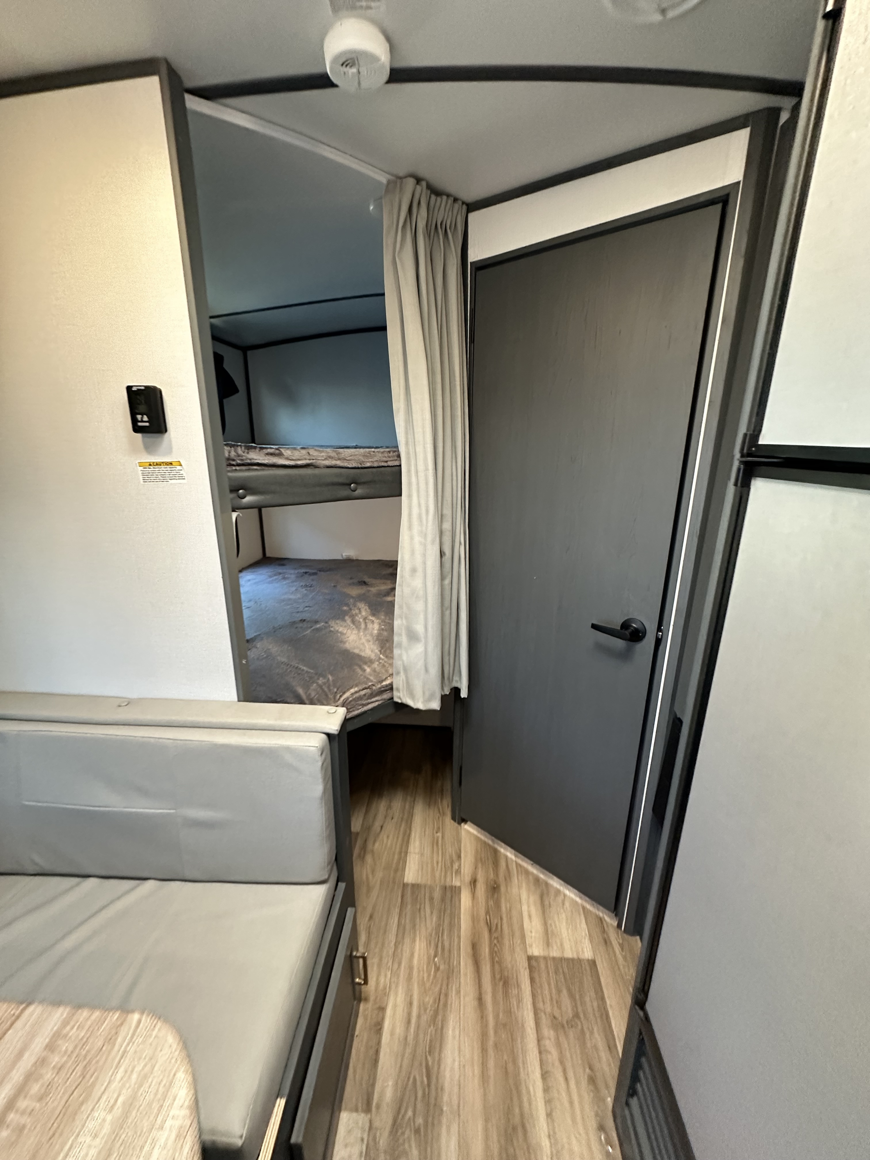 Inside a modern RV rental: A smart layout with bunk beds behind a curtain, a comfortable sofa, and wood-look flooring.. Keystone RV Bullet Ultra Lite 2023