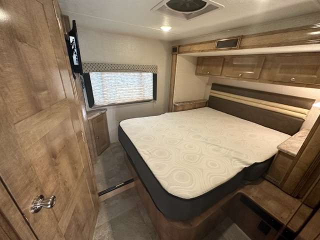 Modern RV rental bedroom with a cozy bed, overhead cabinets, window, and TV. A comfortable space for your travels.. Forest River Coachmen Leprechaun 2020