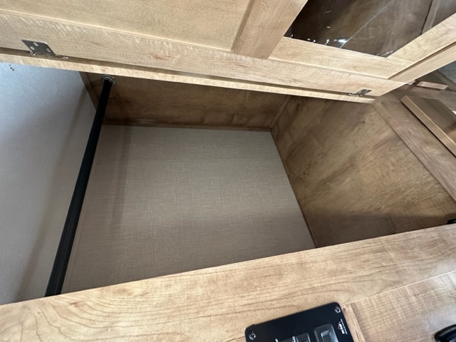 Clean overhead storage cabinet in an RV rental, featuring wood interior, fabric base, and left support rod.. Forest River Coachmen Leprechaun 2020