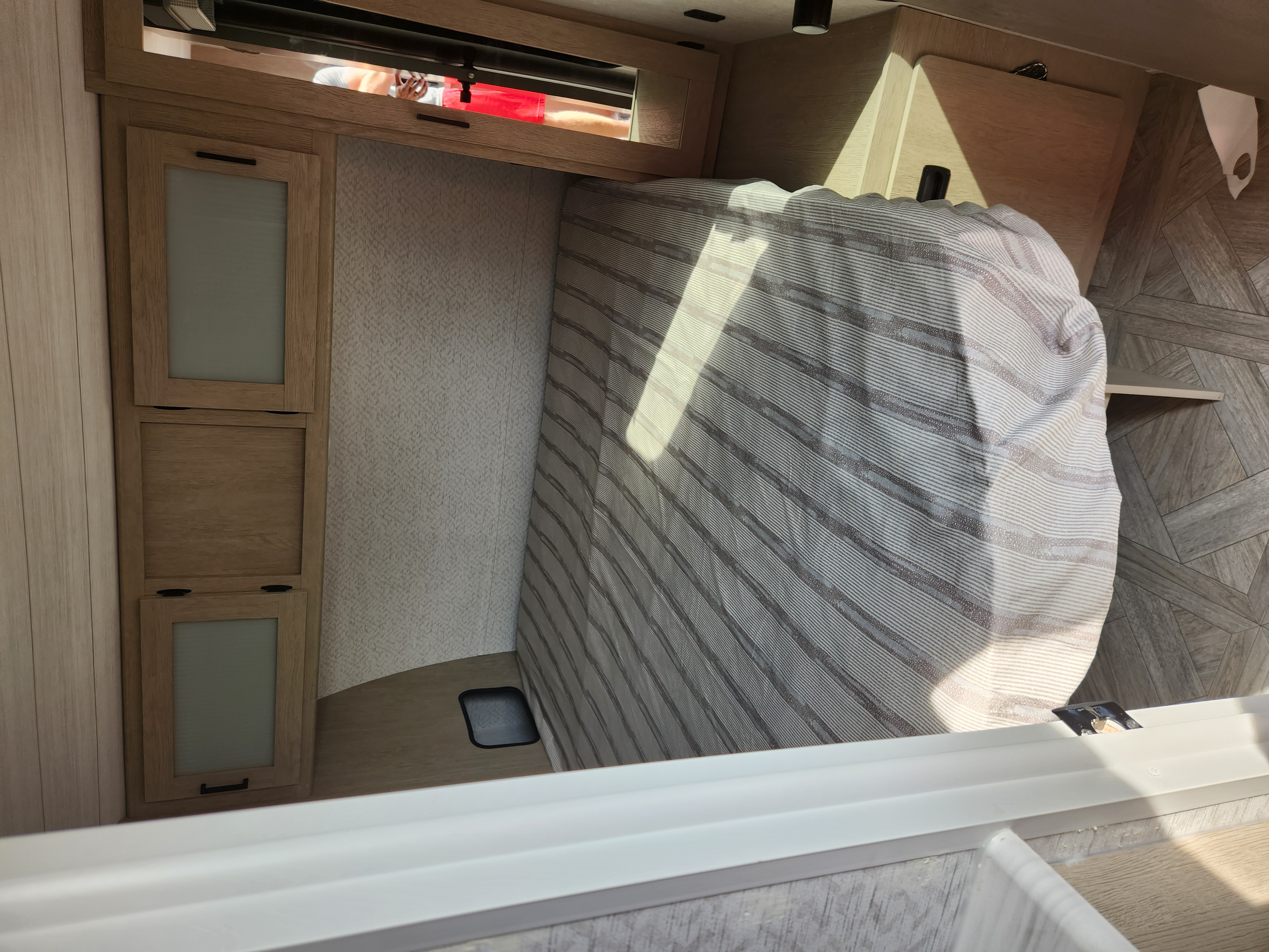 Cozy RV rental bedroom with striped bed, sleek wooden cabinets, and geometric wallpaper, illuminated by sunlight.. Forest River Wildwood 2023