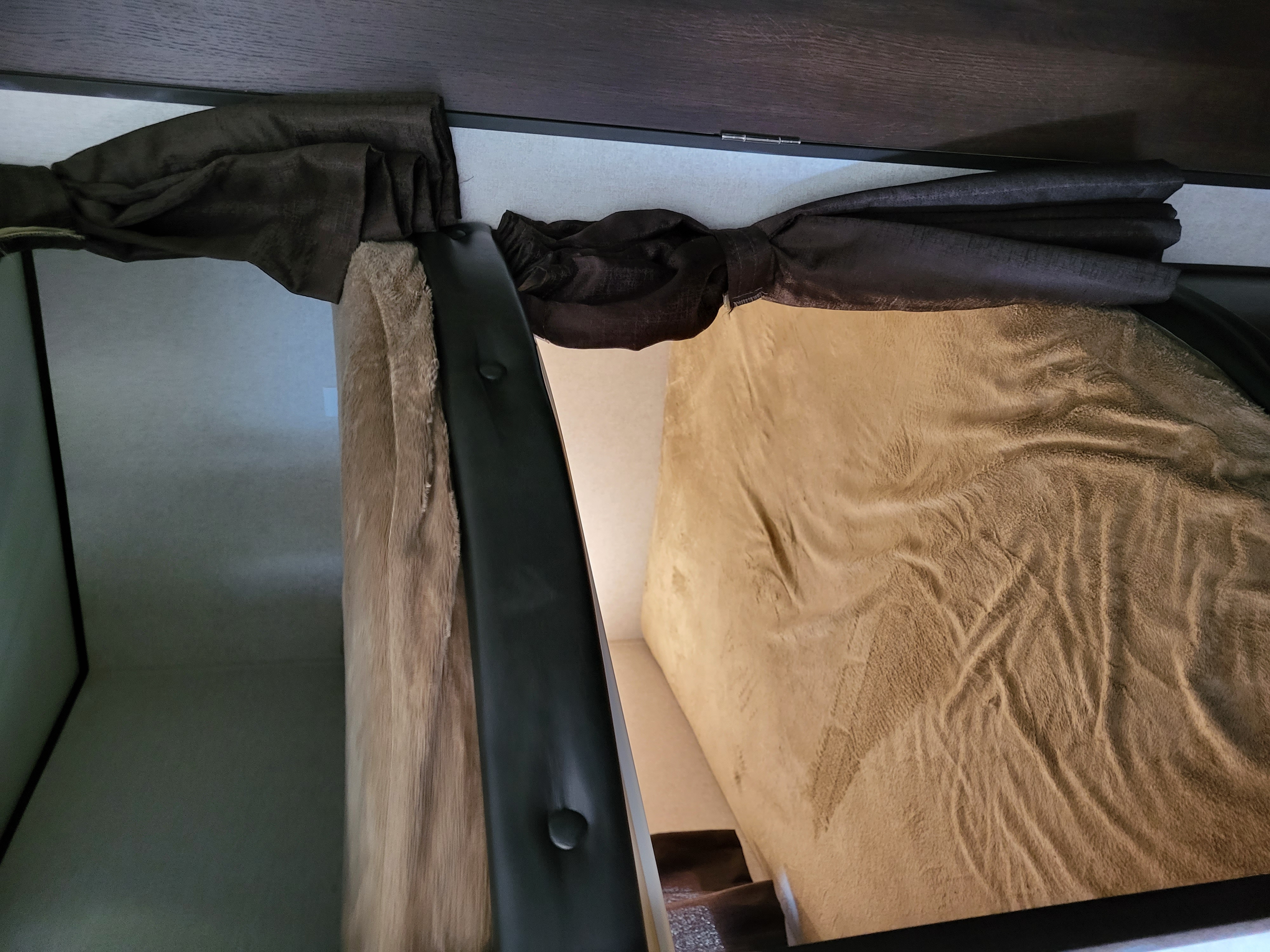 Cozy bunk bed area in an RV rental, featuring a tan blanket and dark brown curtains, perfect for comfortable travel.. Jayco Jay Flight 2018