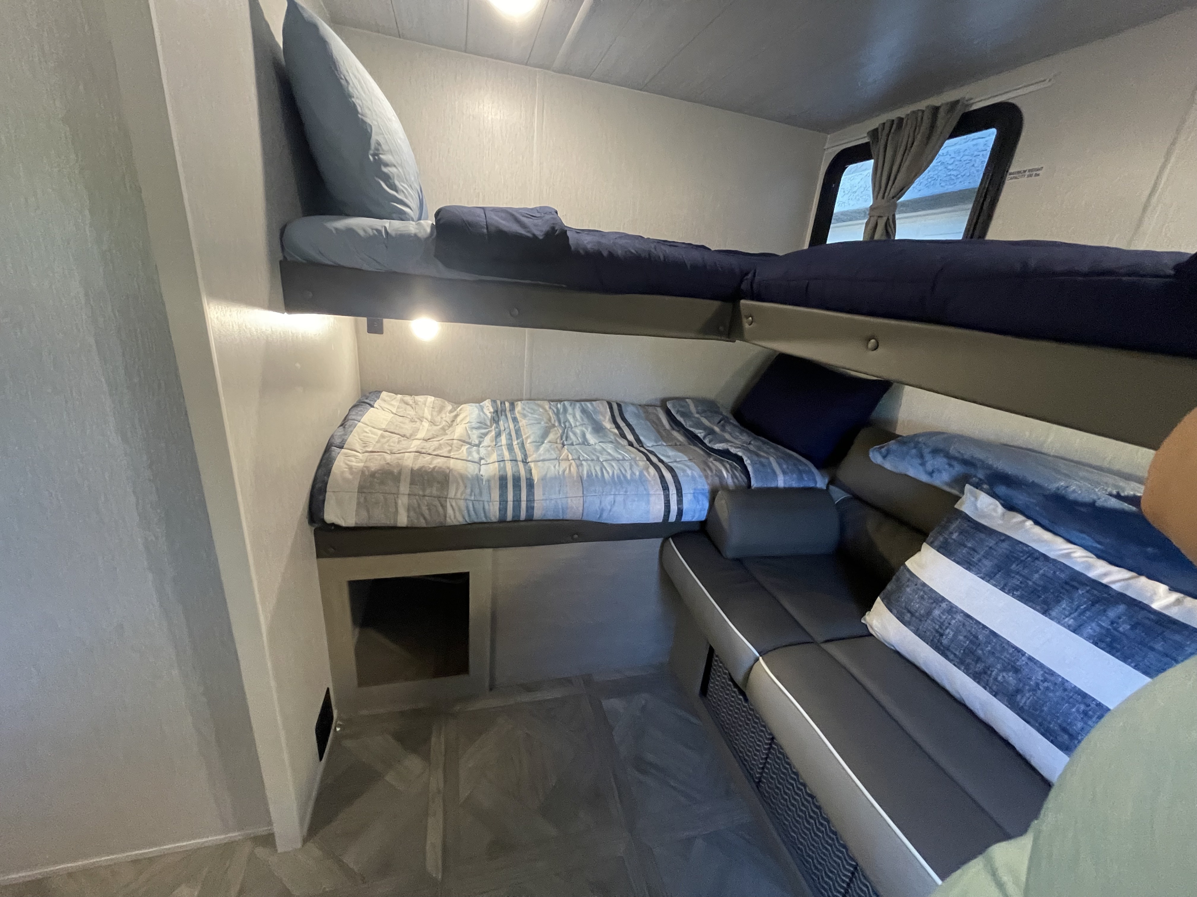 Cozy RV rental interior featuring bunk beds, a sofa, and a window, ideal for comfortable family sleeping.. Forest River Wildwood X-Lite 2023