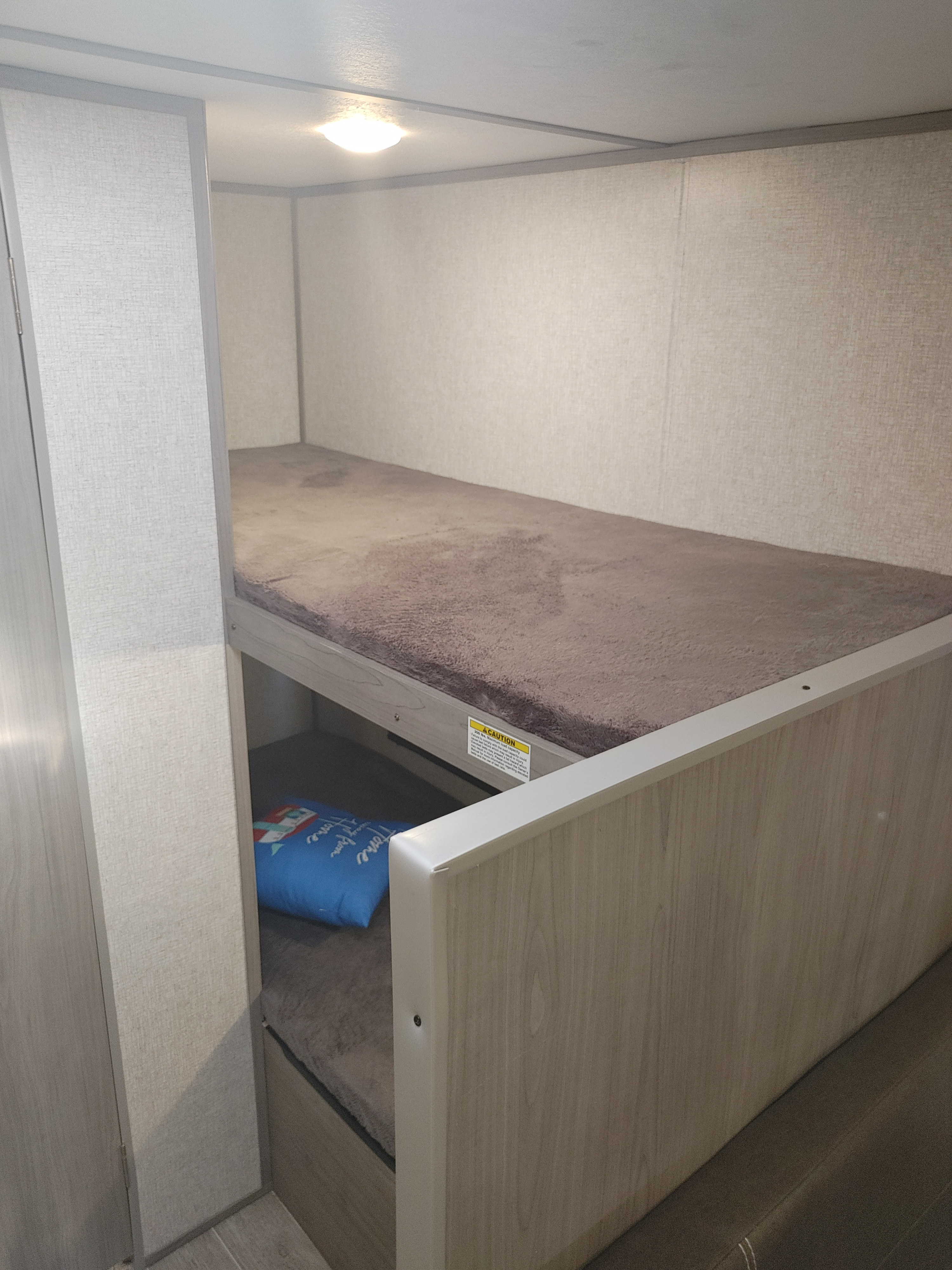 Cozy bunk beds in an RV rental, featuring a top bunk with a soft mattress cover and a blue pillow on the bottom bunk, all within a light-colored interior.. Coleman 17B 2022