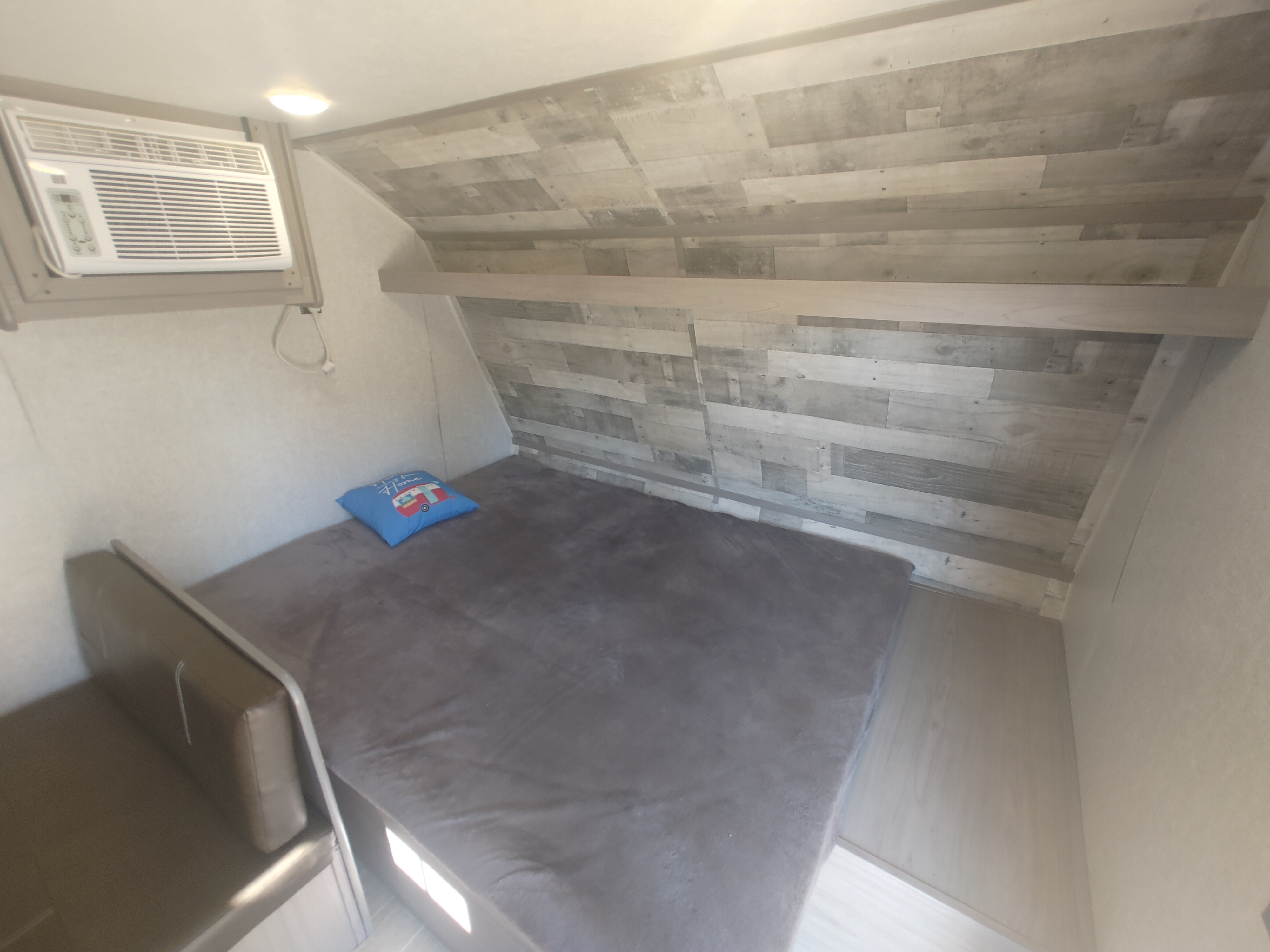 RV rental: A cozy sleeping area inside, featuring a bed with a blue pillow, air conditioner, and wood-paneled accent wall.. Coleman 17B 2022