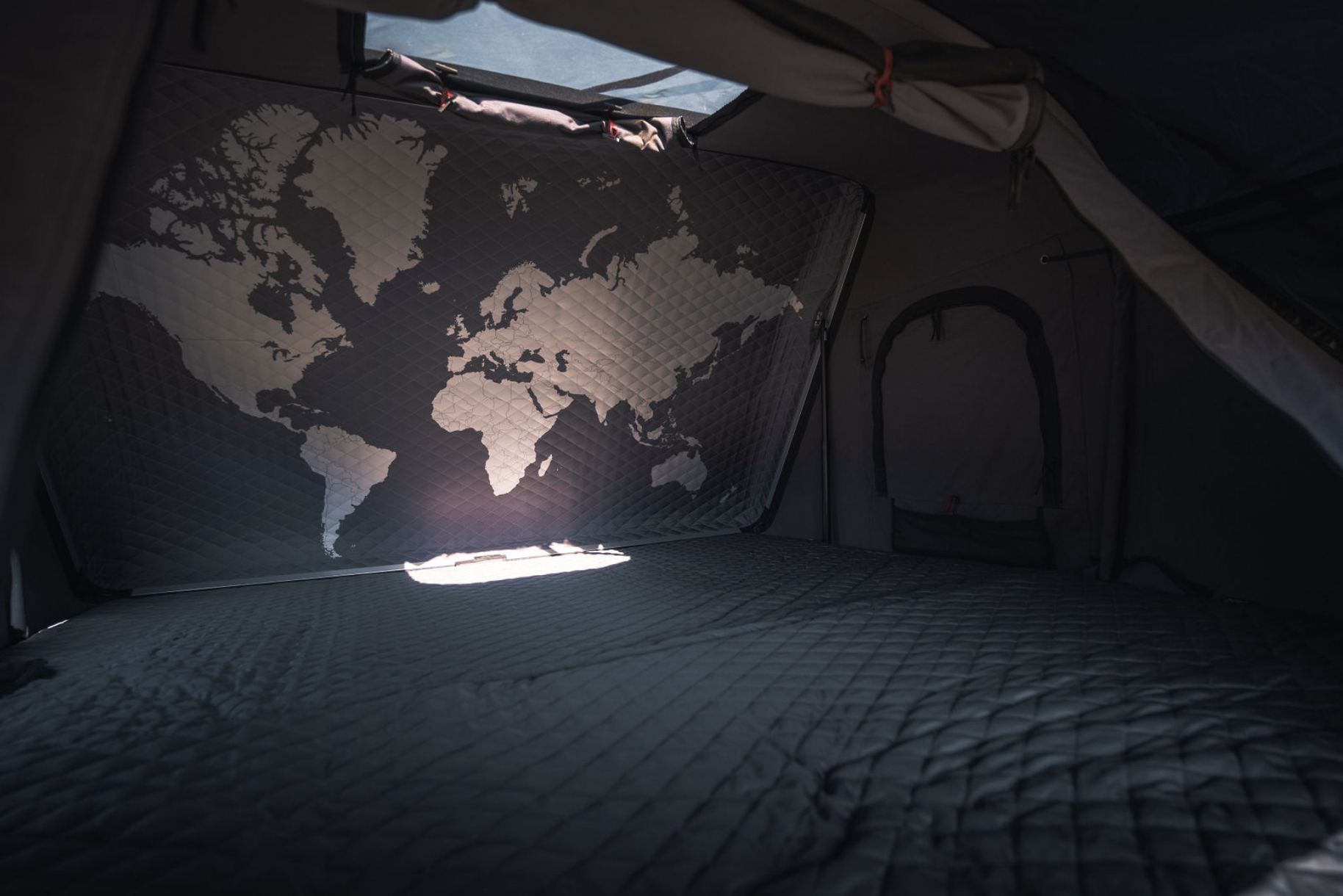 Interior of an RV rental: a quilted world map spans the back wall above a soft bed, inviting travels and camping adventures.. Toyota Tacoma 2023