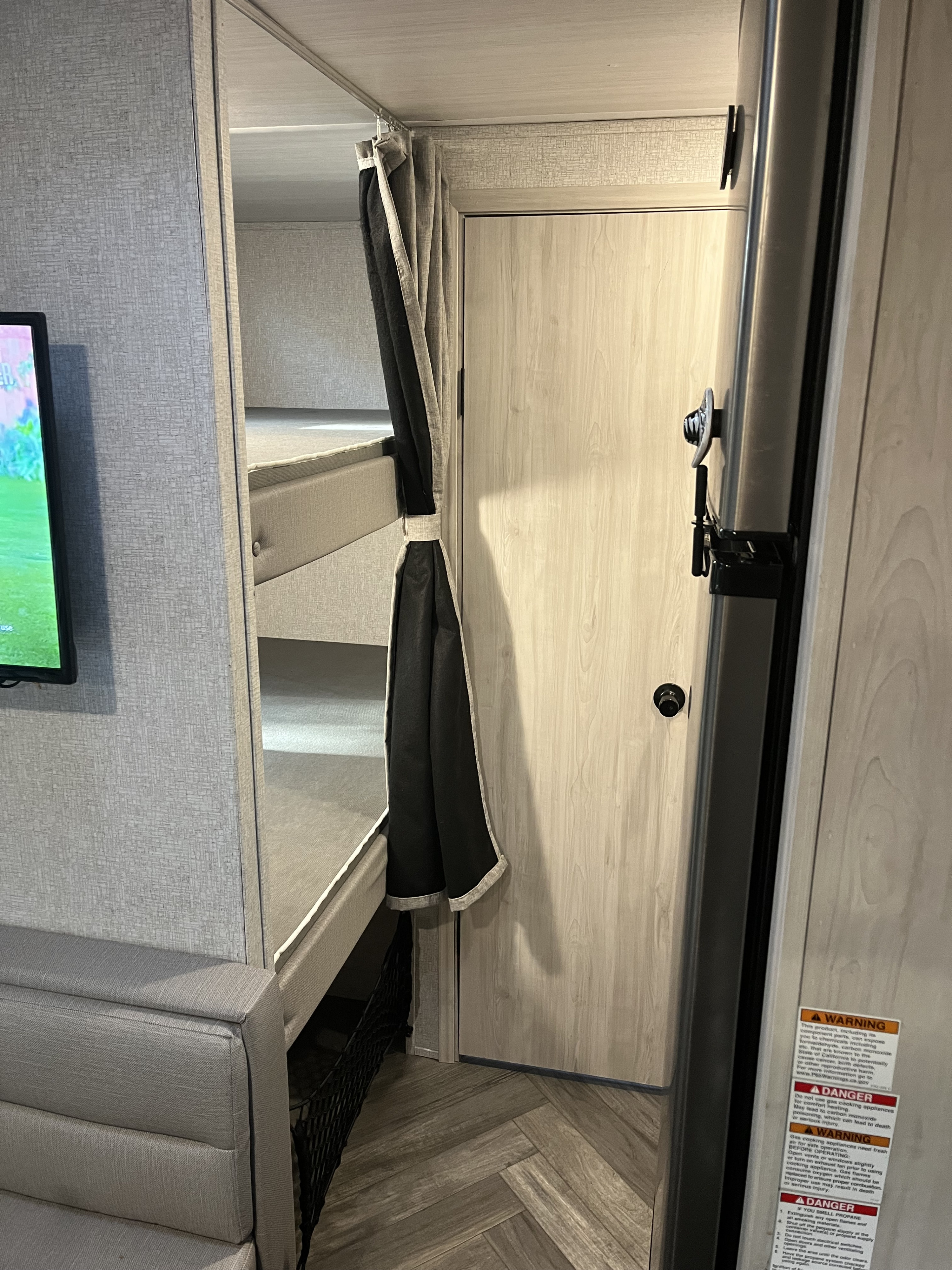 Inside an RV rental: cozy bunk beds with privacy curtain, TV, and light wood interior, perfect for compact living.. East to West Della Terra 2022