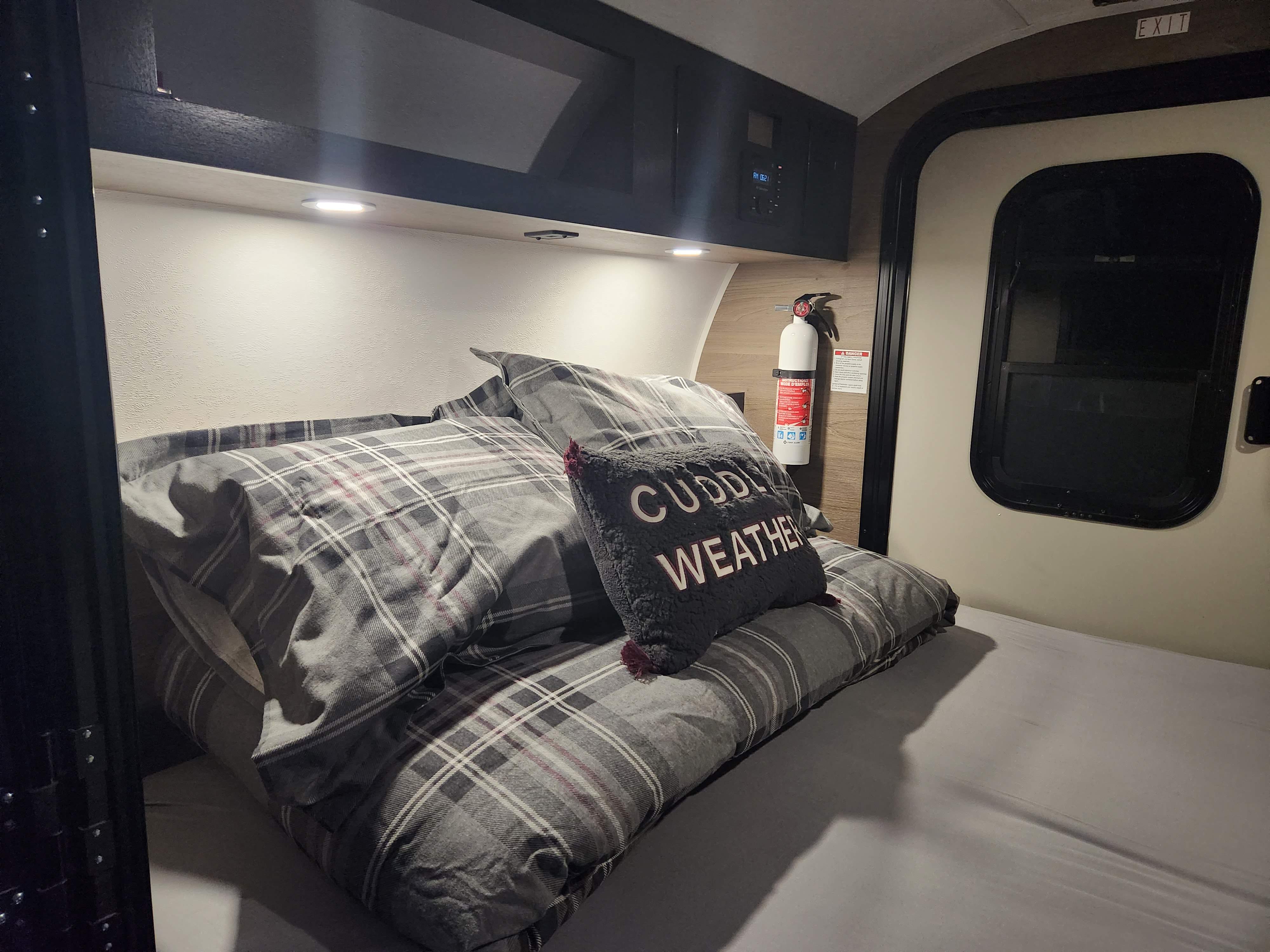 Cozy RV rental bedroom with plaid bedding, "Cuddle Weather" pillow, and essential fire extinguisher.. Braxton Creek Bushwacker 2023
