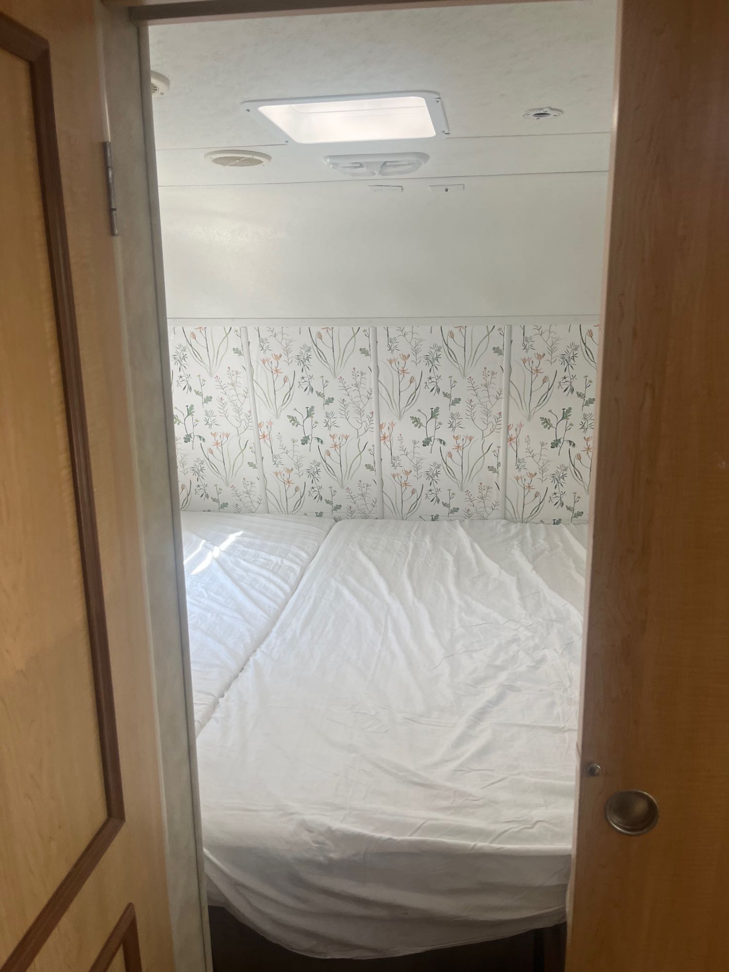 Cozy RV rental bedroom featuring floral decor, comfortable white bedding, and bright overhead lighting. Ready for adventure.. Spree Spree Trailer 2008