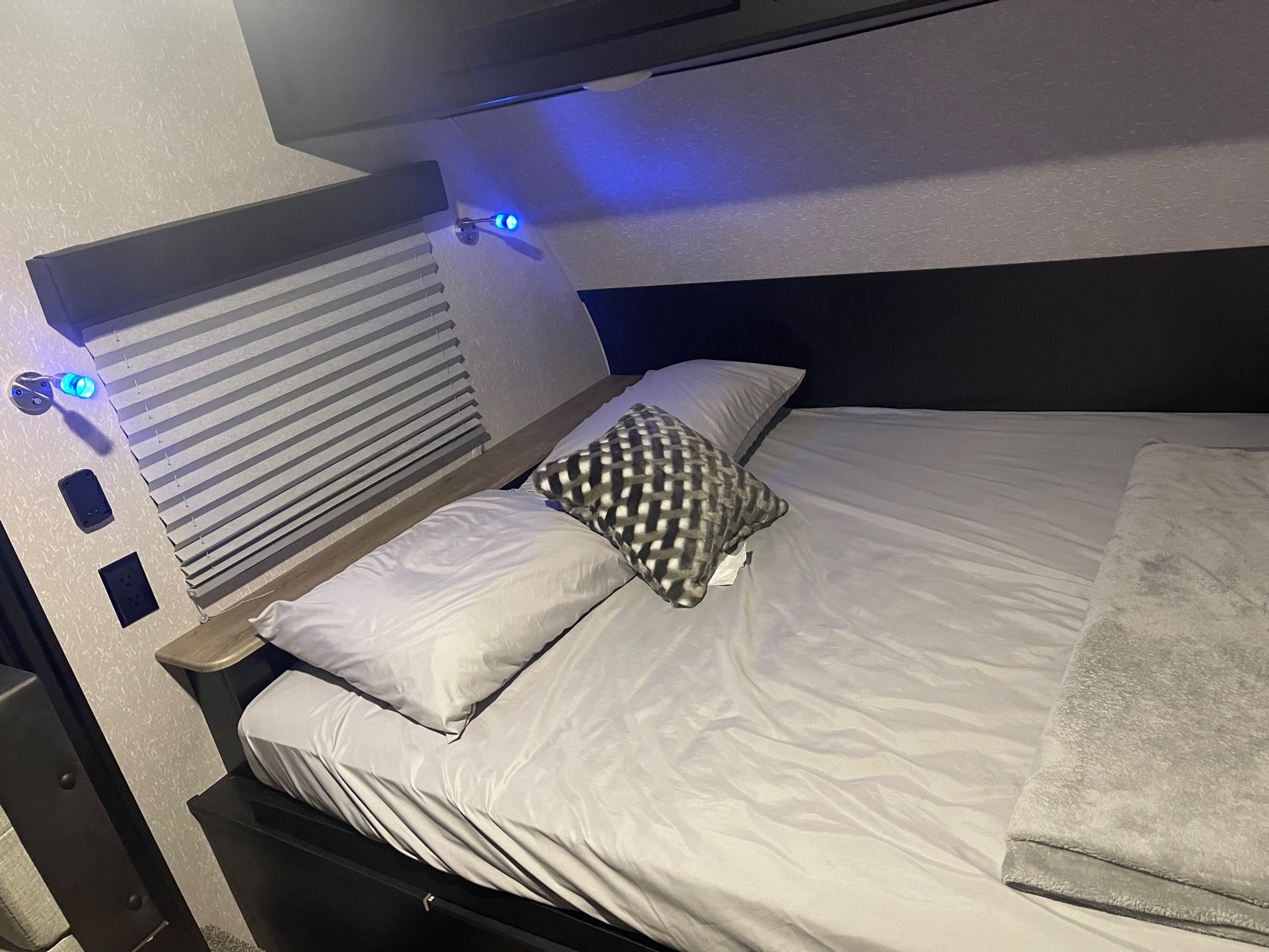 Cozy RV rental bedroom featuring a comfy bed with blue accent lights, pillows, and a window with shades.. Forest River Cherokee Wolf Pup Black Label 2022