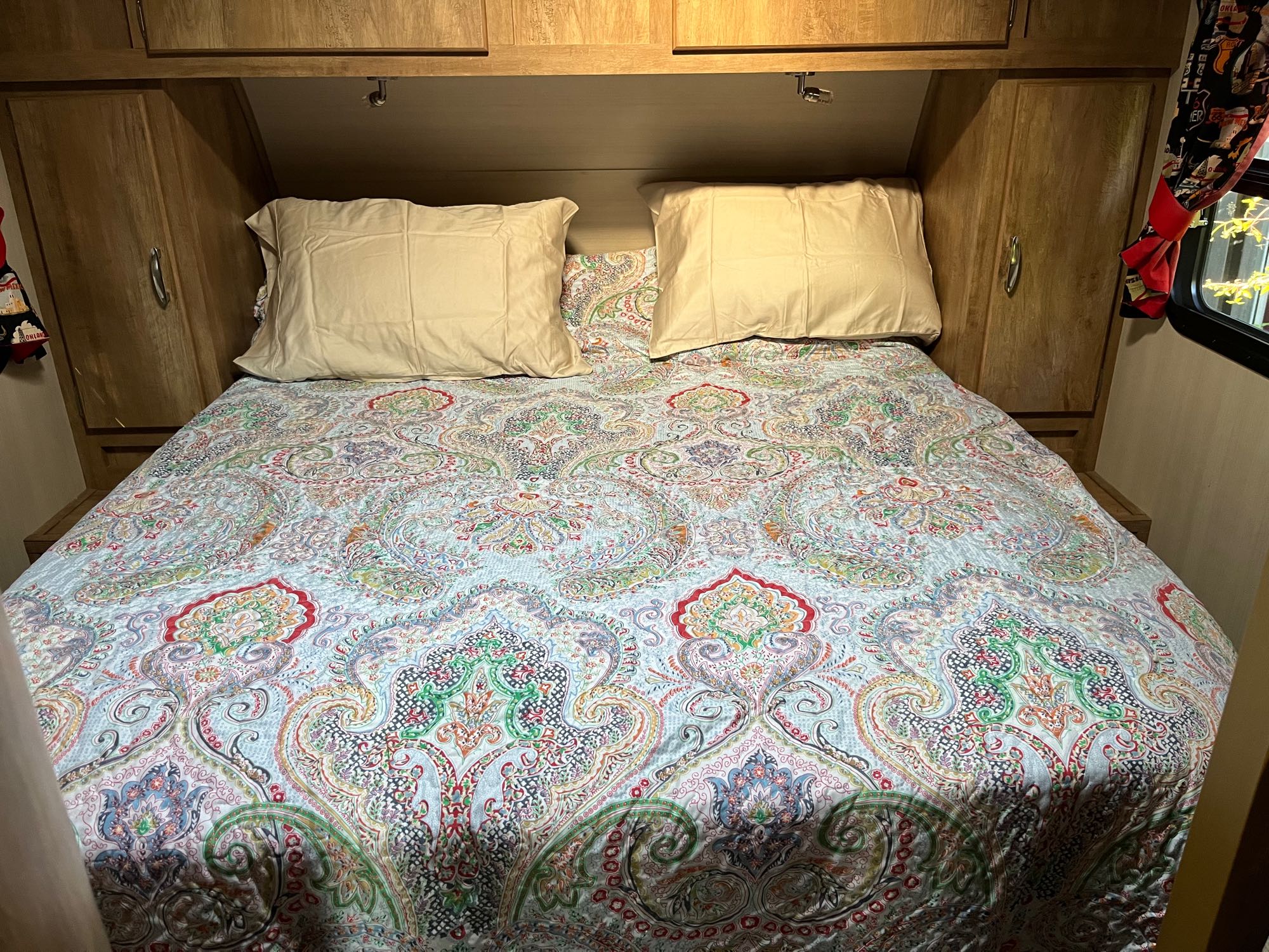 Cozy RV rental bedroom with colorful paisley quilt, pillows, and wooden storage.. Gulf Stream Vintage Cruiser 2017