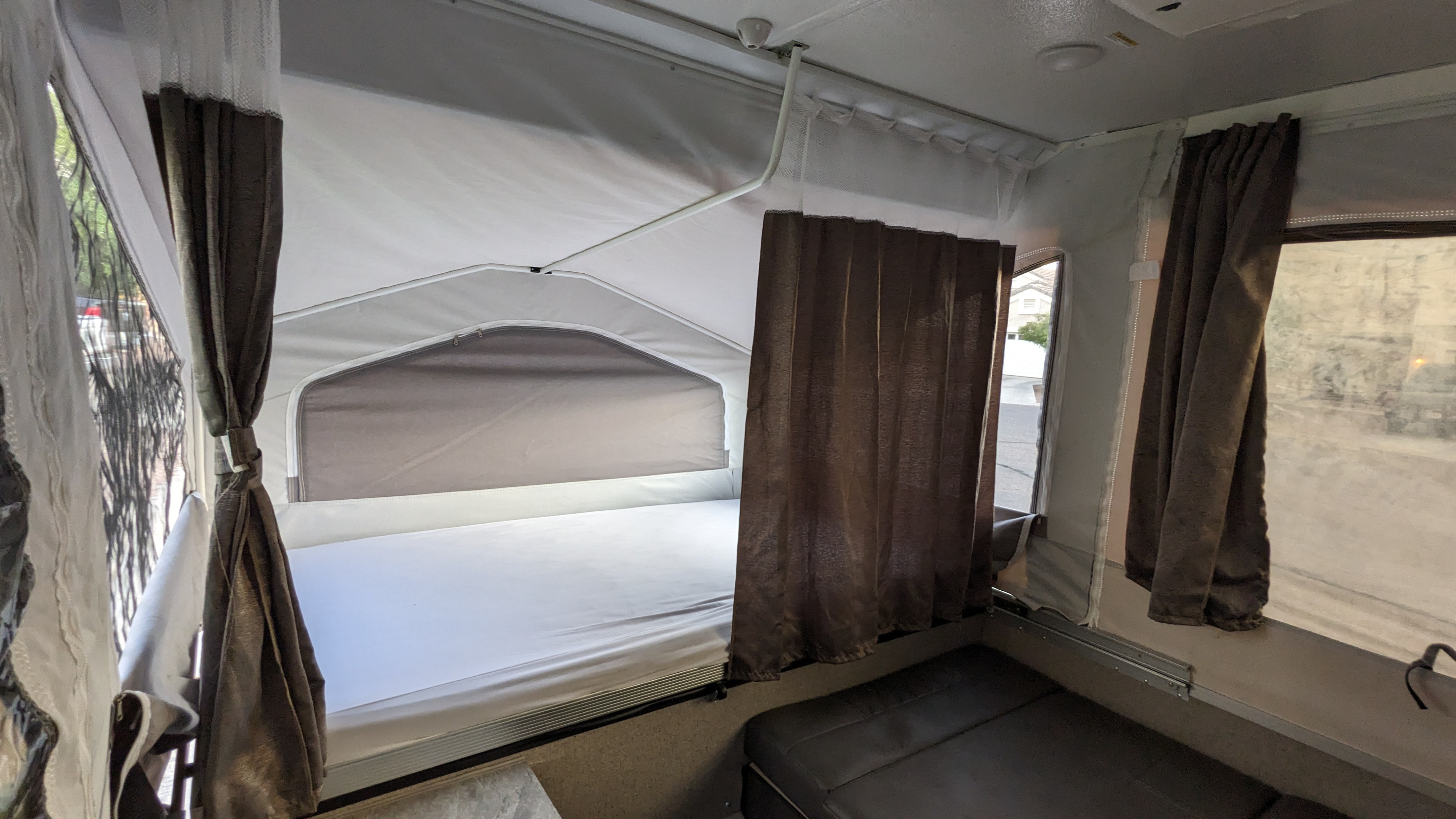 Cozy pop-up RV rental interior with a bed, white sheets, dark curtains, and a sofa.. Forest River Flagstaff M.A.C. 2021