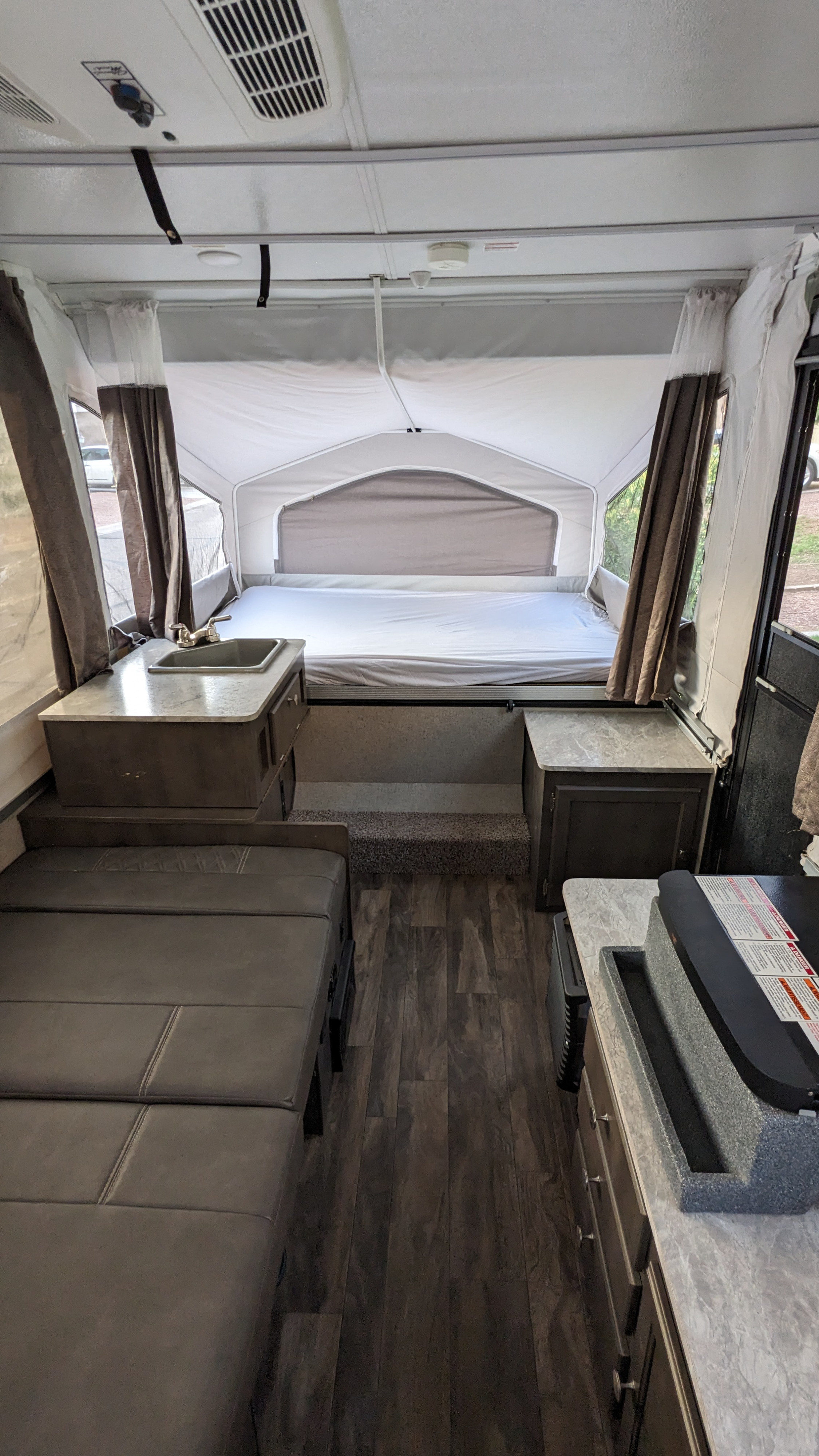 RV rental pop-up camper interior, showing the bed, kitchen with sink/stove, and a dinette. Dark wood floors & light walls.. Forest River Flagstaff M.A.C. 2021