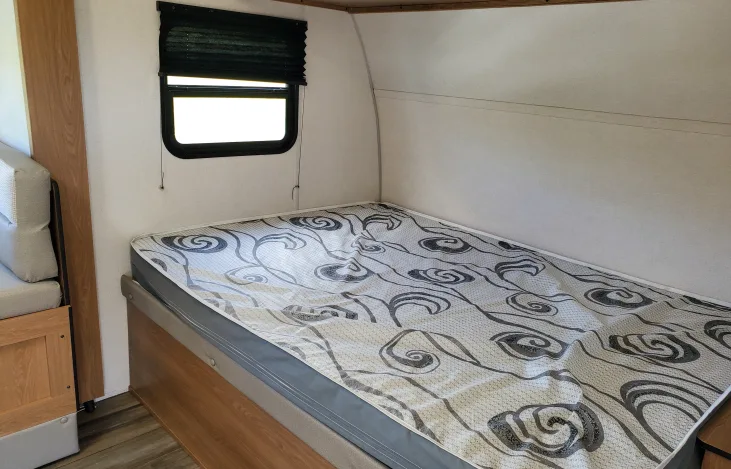Inside an RV rental: a cozy bedroom nook with a patterned mattress, window, and compact design for travelers.. Avenger LT 2022