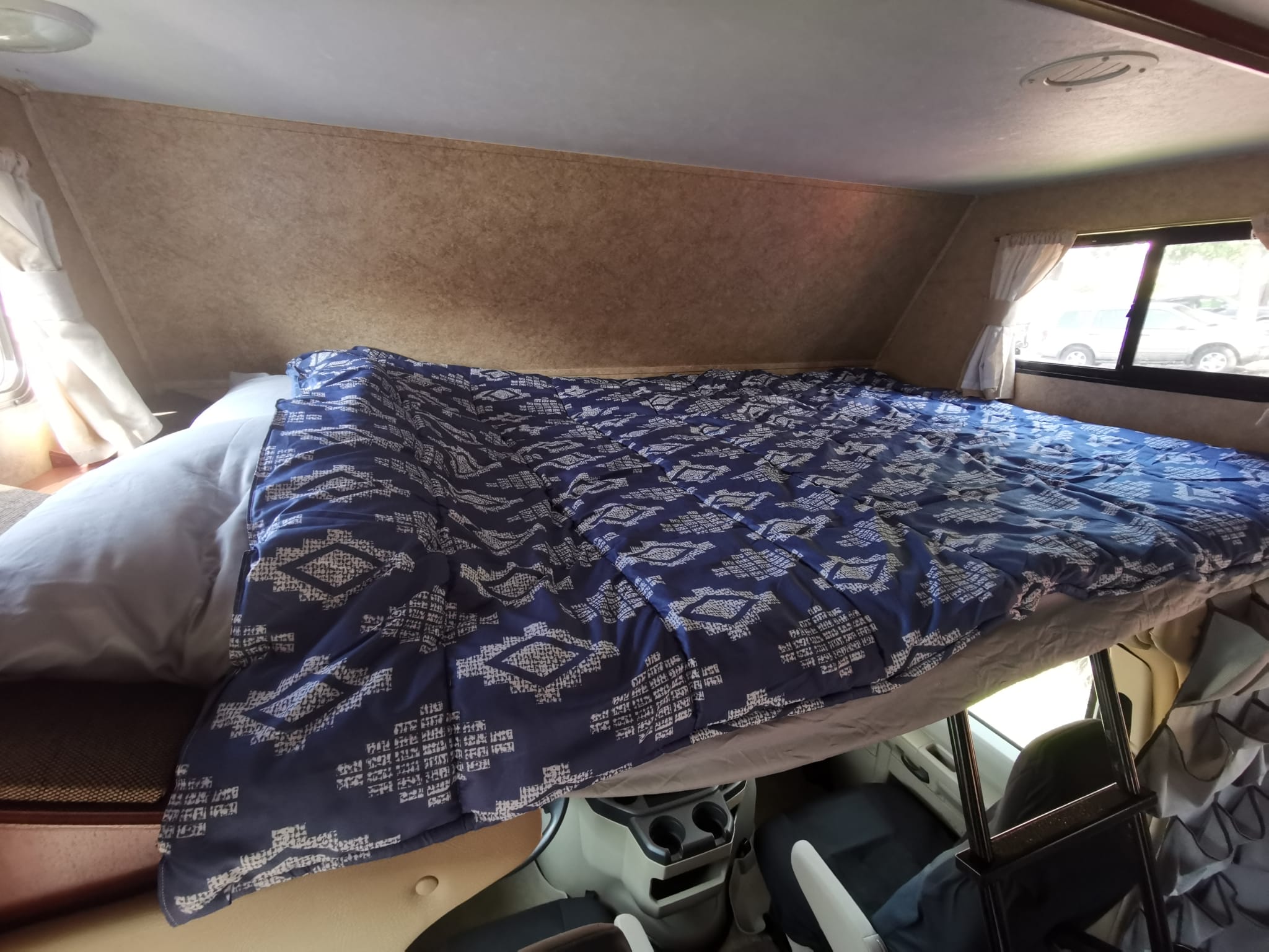 Inside an RV rental: a comfortable over-cab bunk bed with a blue patterned comforter, offering a cozy sleep space.. Forest River Sunseeker 2010