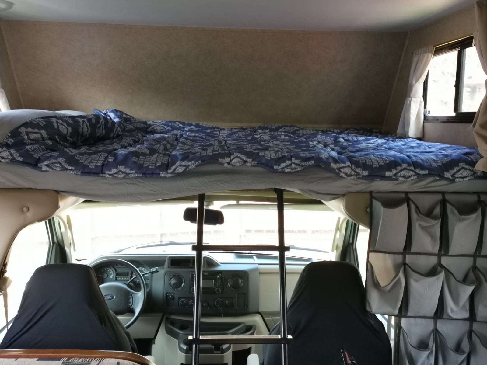 Cozy RV rental interior featuring an overhead bunk bed with bedding, a ladder, and front cab.. Forest River Sunseeker 2010