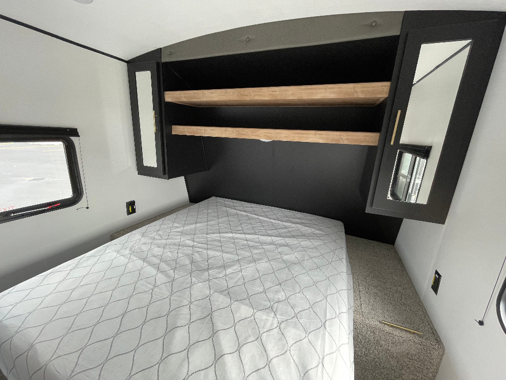 RV rental: Bright bedroom interior with a comfortable bed, overhead shelving, and mirrored cabinets.. Keystone RV Springdale 2021