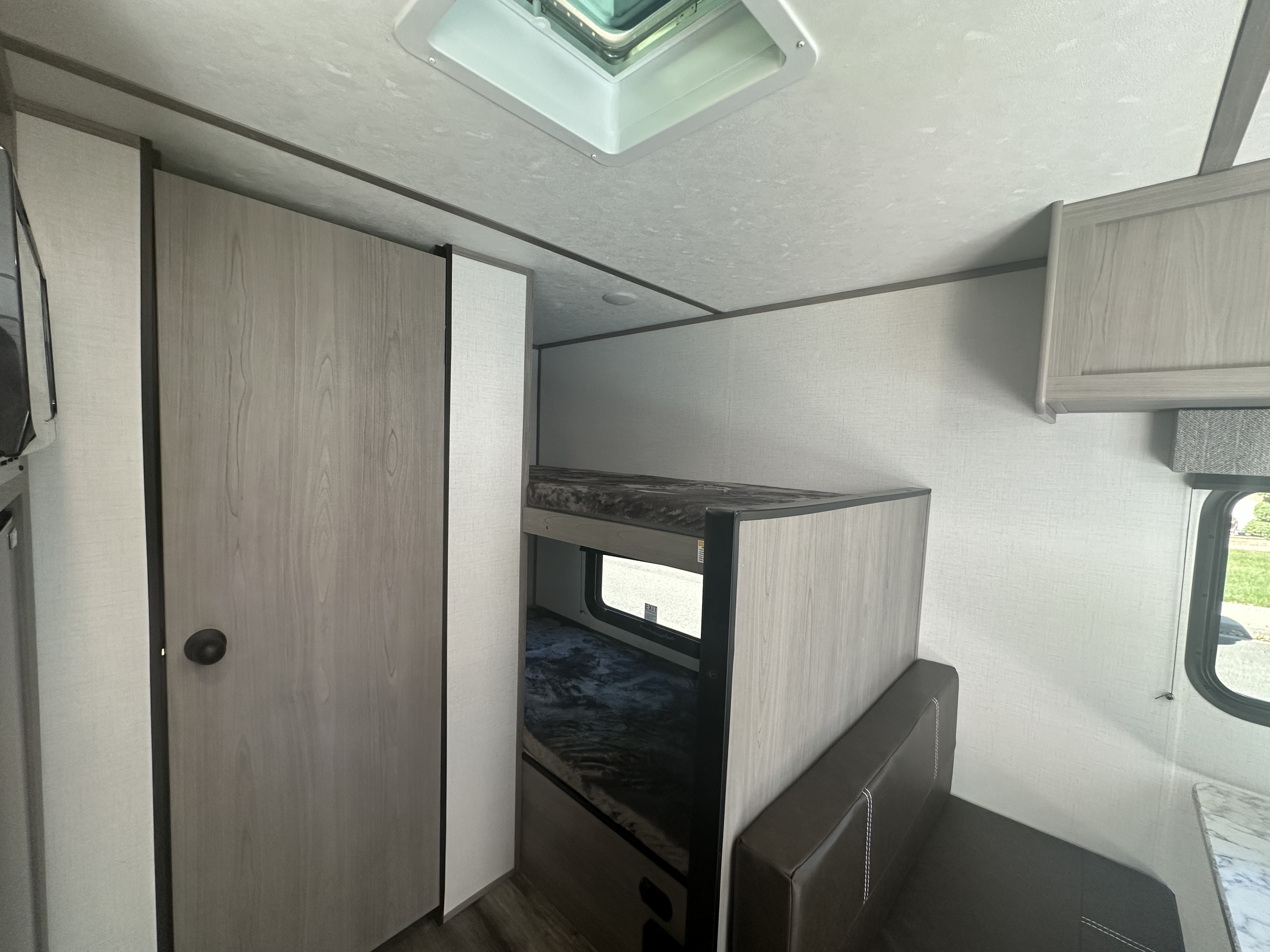 Inside RV rental: bunk beds, dinette seating, and light wood cabinetry with a skylight. Ideal for comfortable travel.. Dutchmen Coleman Lantern LT 2023