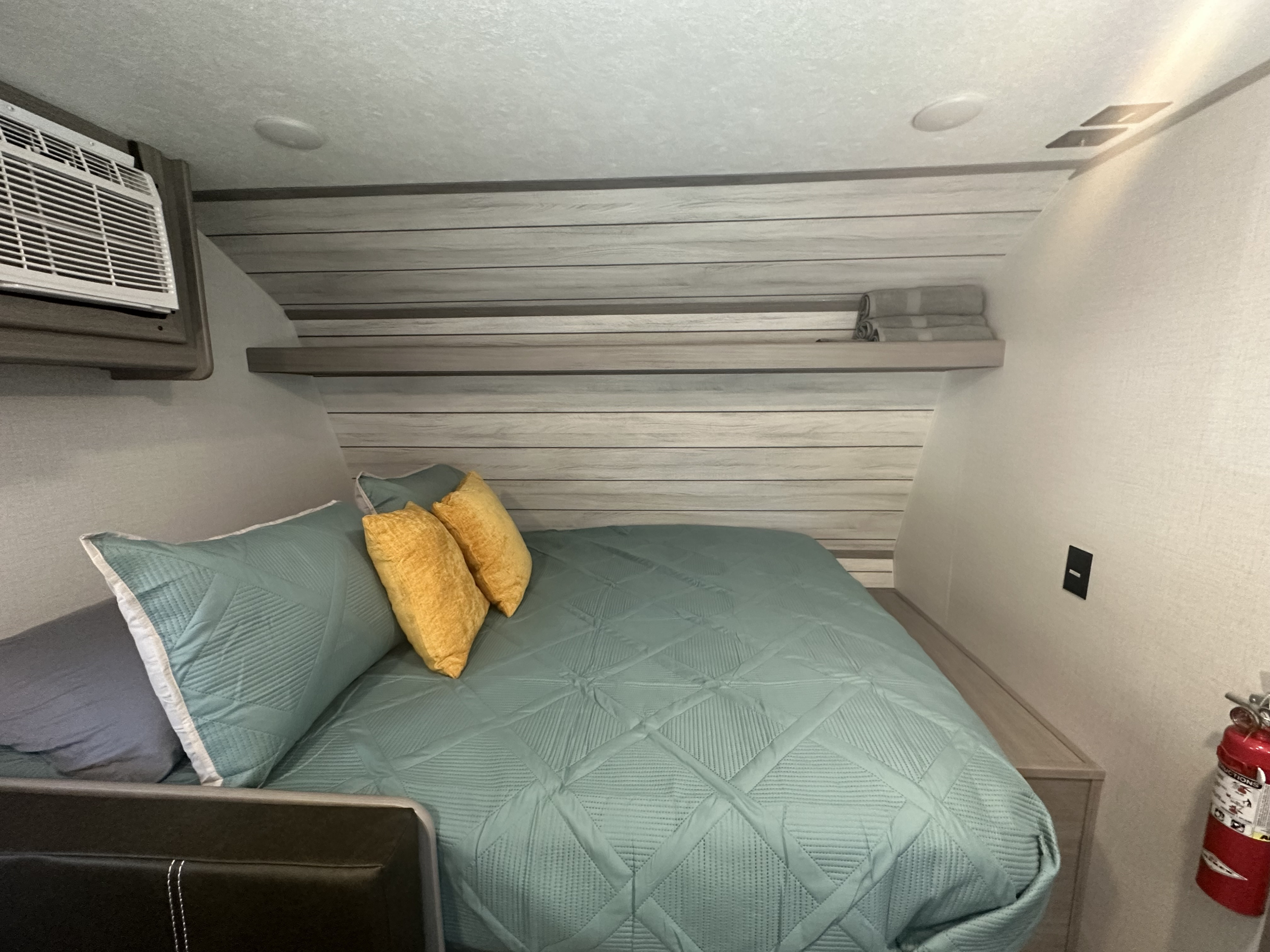 Cozy RV rental bedroom with a teal bed, A/C unit, overhead shelf, and fire extinguisher, ready for your travels.. Dutchmen Coleman Lantern LT 2023