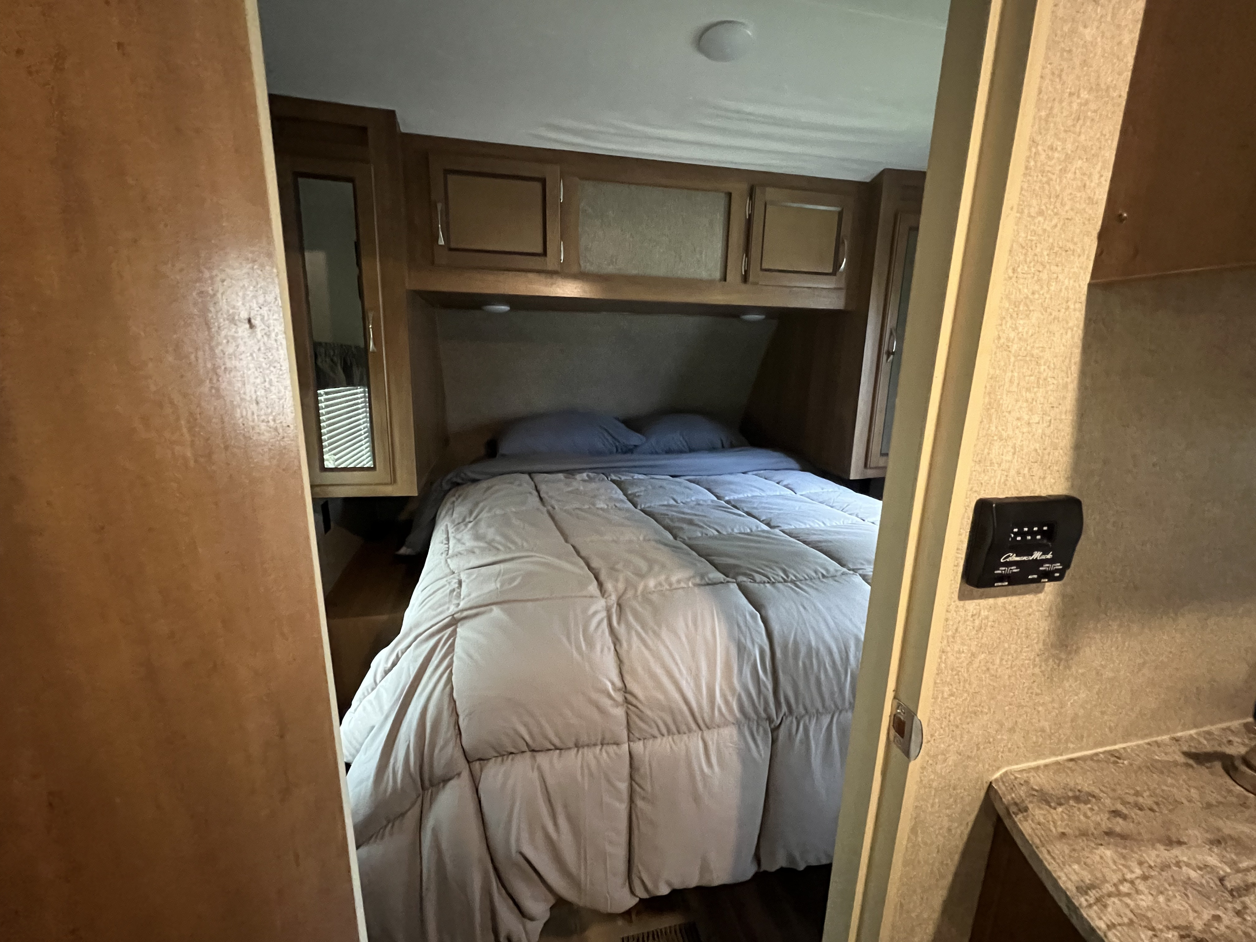 Experience comfort in this RV rental's cozy bedroom. It features a bed with overhead cabinets & a side window.. Coachmen 273BHS 2019