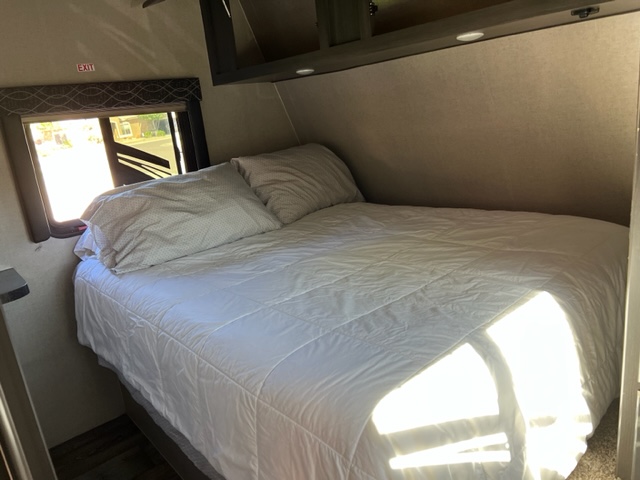Comfortable RV rental bedroom with white bed, window, and overhead cabinets. Sunlight streams in.. Genesis Supreme Rv Genesis Supreme 2019