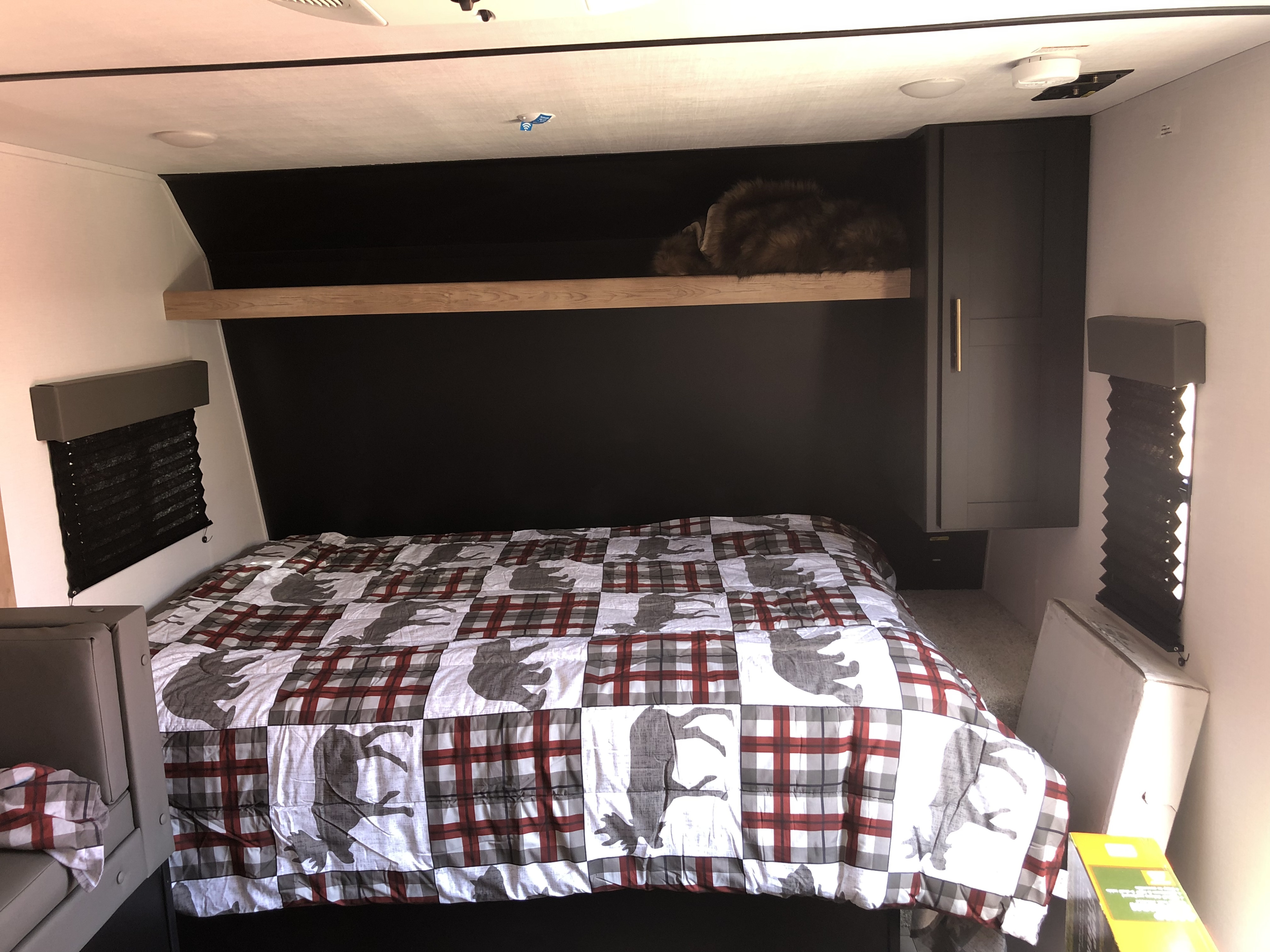 Cozy RV rental bedroom with patterned bedding, a cat napping on the shelf, window blinds, and cabinet storage.. Keystone RV Springdale 2022