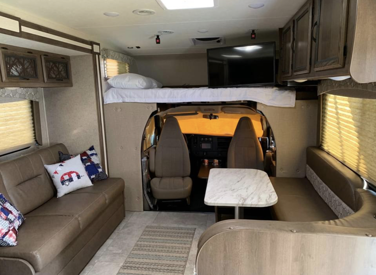 Spacious RV rental interior featuring a comfortable living area with a couch, dinette, and an overhead bed above the driver's cab.. Chevy 4500 2019