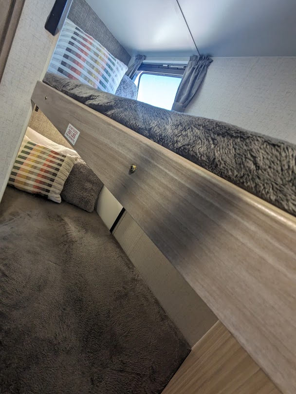 RV rental's cozy interior features comfortable bunk beds with soft gray blankets, pillows, and a window view.. Winnebago Micro Minnie 2022
