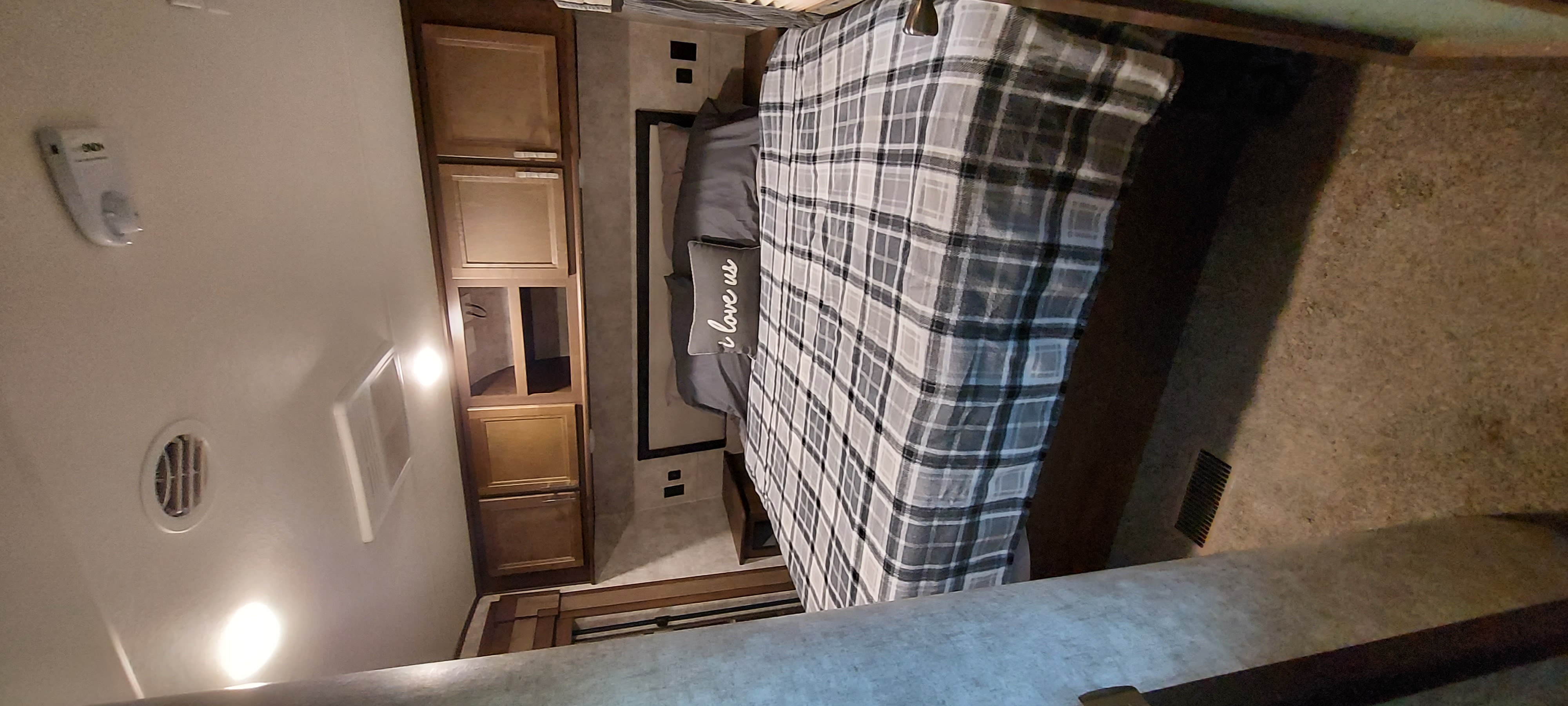 Cozy RV rental bedroom featuring a bed with plaid bedding, 'i love us' pillow, and wooden storage cabinets.. Highland Ridge RV Mesa Ridge 2019