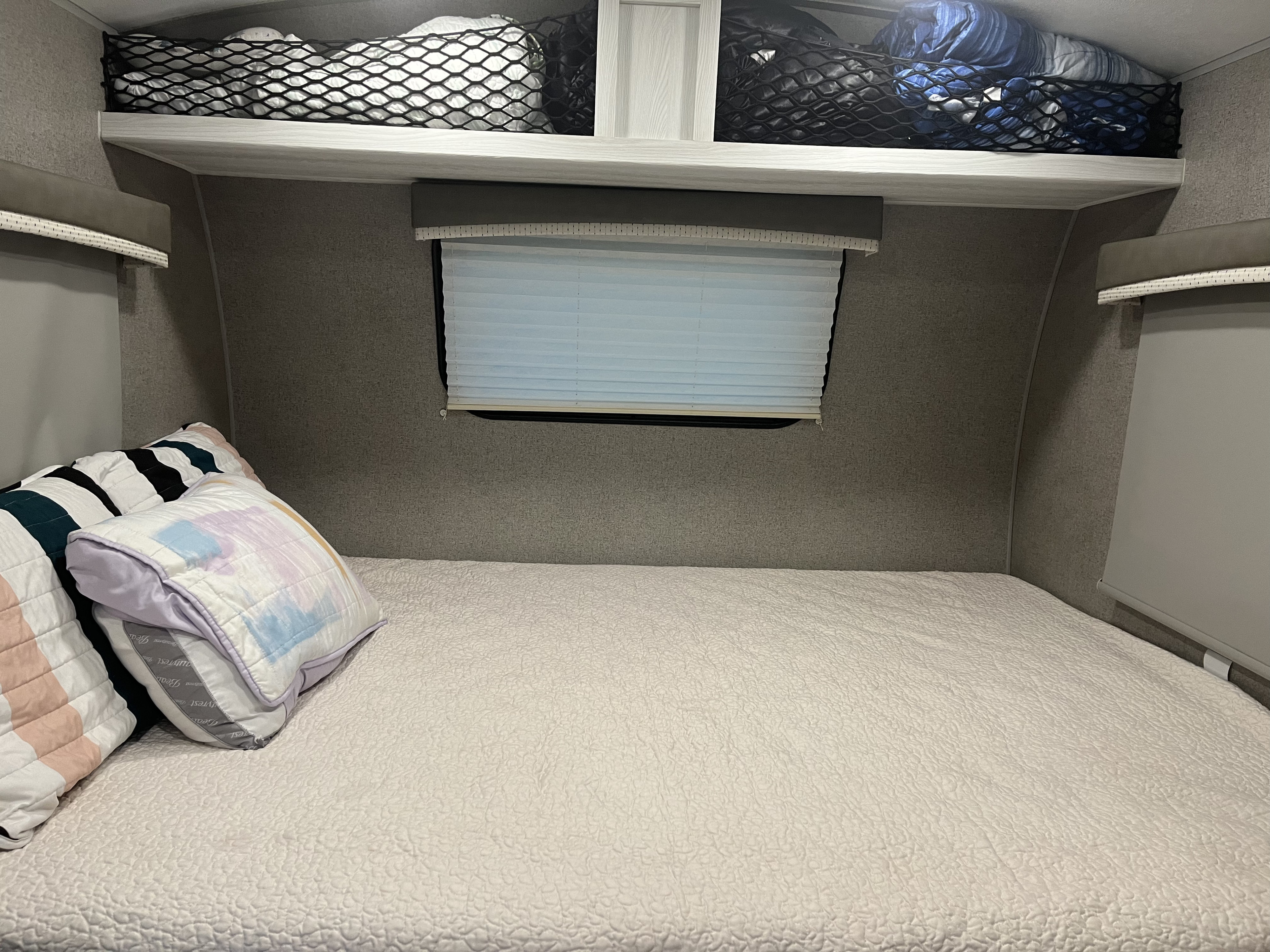 Inside this RV rental bedroom: a quilted bed, overhead storage nets with items, and window blinds for privacy.. Forest River Rockwood Geo Pro 2020