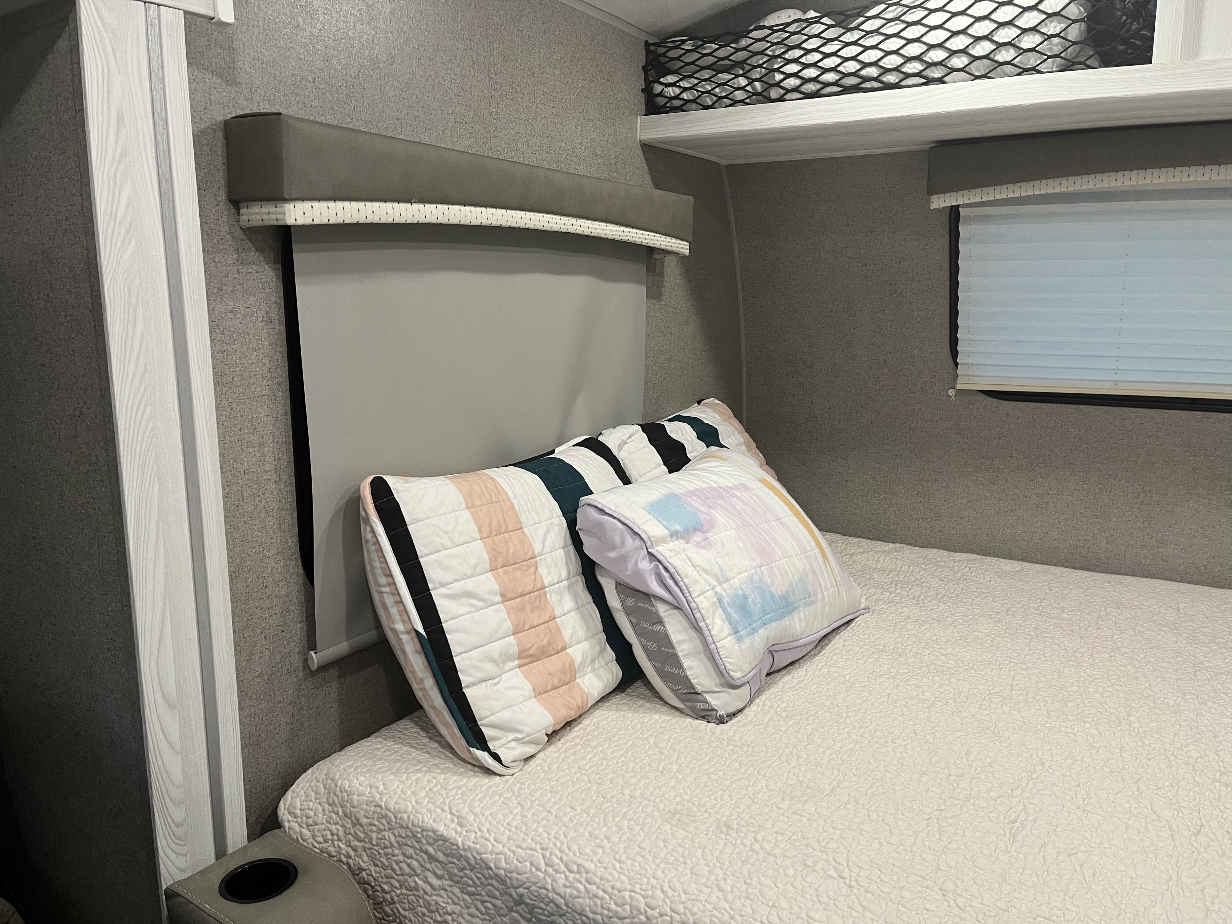 Inside a comfortable RV rental bedroom featuring a bed, decorative pillows, window shades, and overhead storage.. Forest River Rockwood Geo Pro 2020