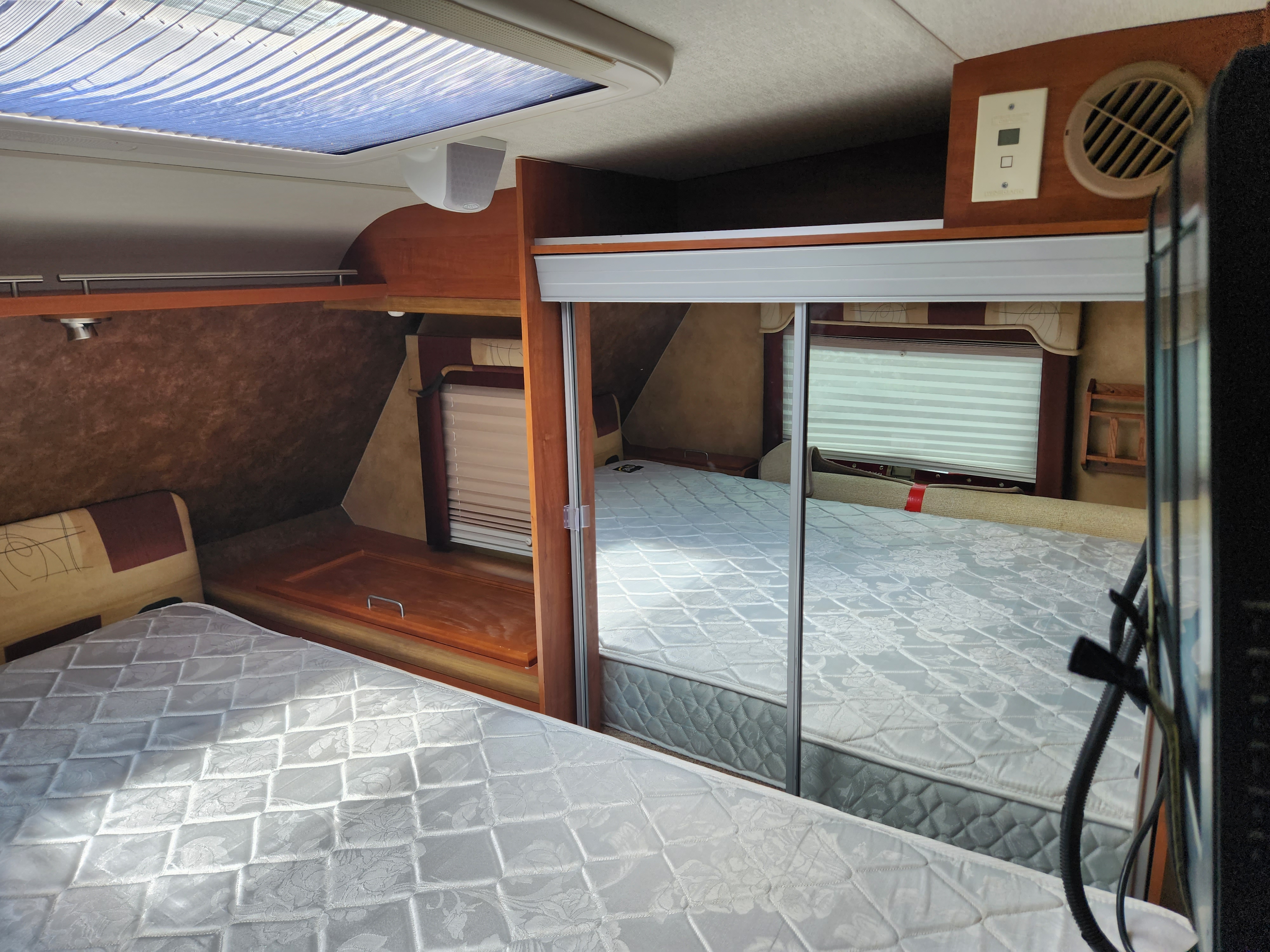 Spacious RV rental sleeping area featuring two white quilted mattresses, an overhead skylight, and mirrored storage.. Dodge Dodge Bighorn 3500 Heavy Duty Pu 2016