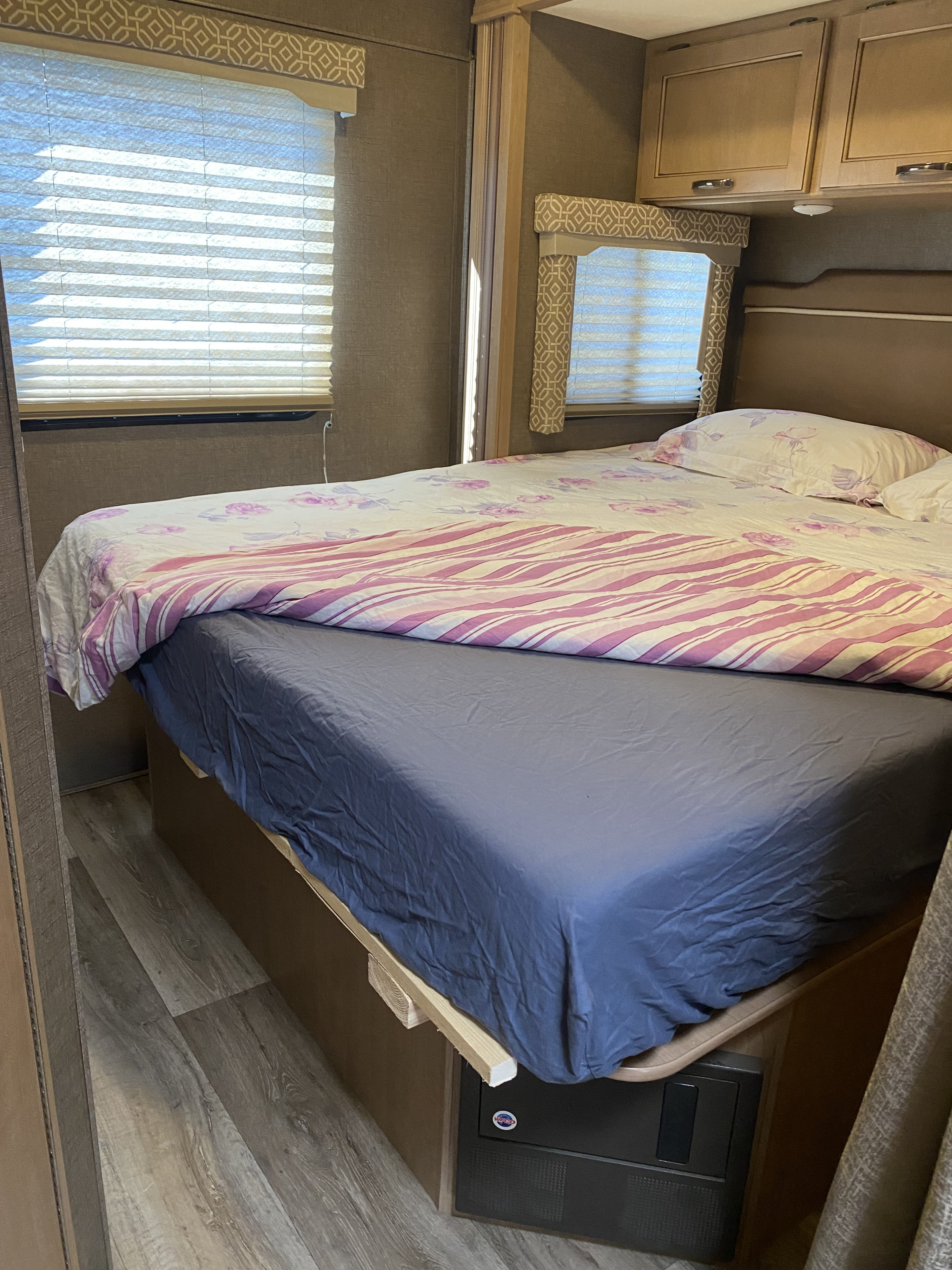 RV rental bedroom showcasing a bed with purple & white bedding, pleated window blinds, and overhead cabinets.. Thor Freedom Elite 2019