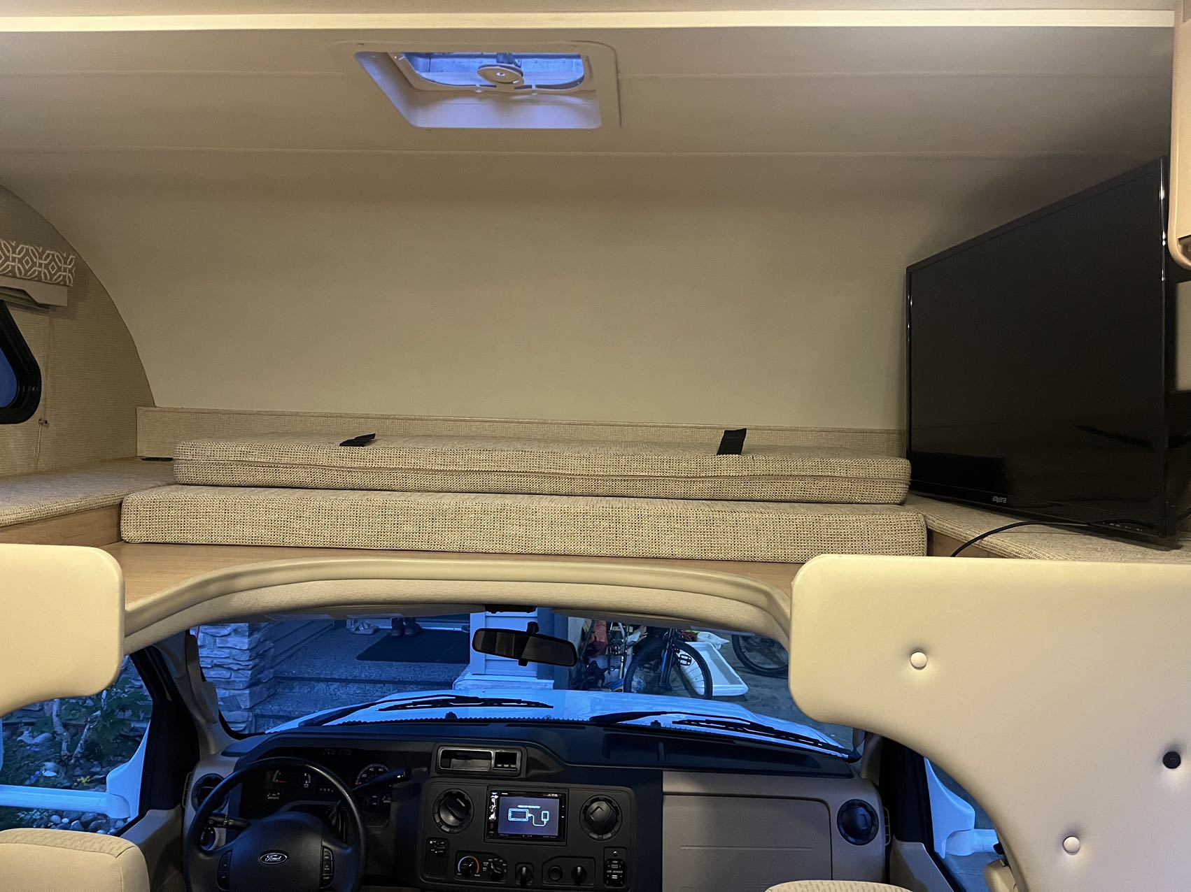 Inside an RV rental: the cozy cab-over bunk, dashboard, TV, and the outside view from the windshield.. Thor Freedom Elite 2019