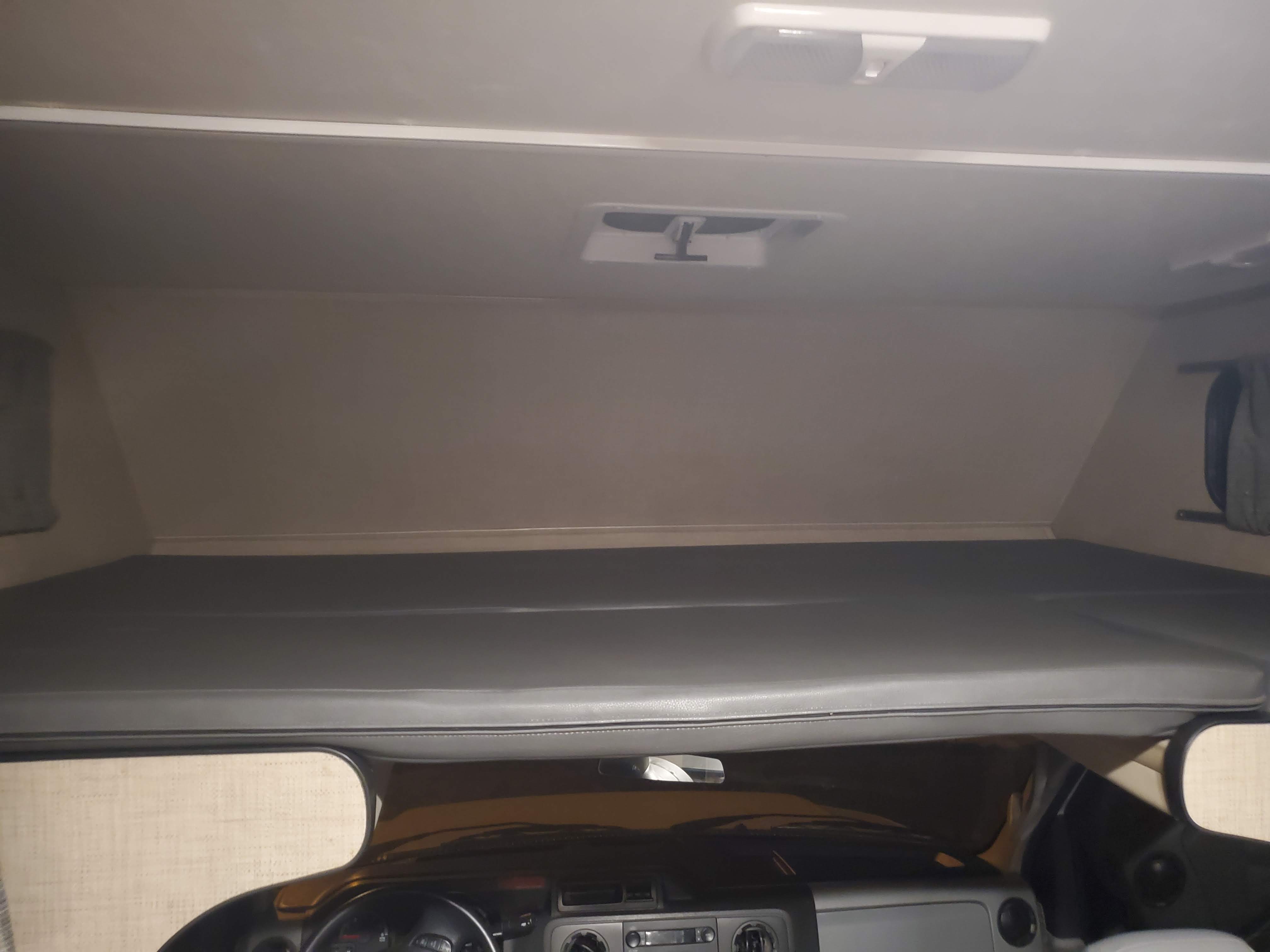 View inside an RV rental, featuring the comfortable cab-over sleeping area directly above the driver's console.. Thor Majestic 2019